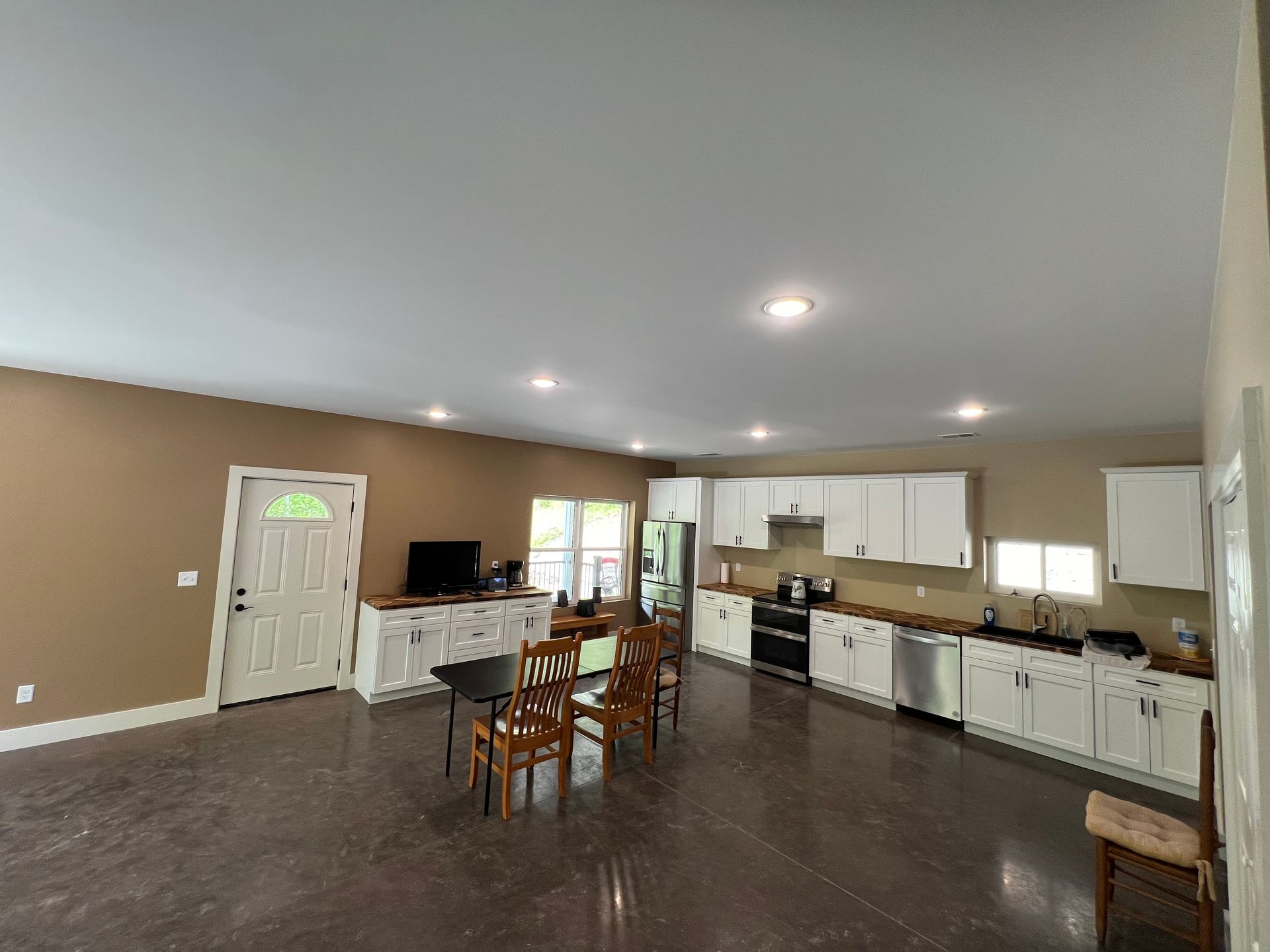 An open-concept kitchen and dining area with white cabinets, stainless steel appliances, and a brown wall. A table and chairs are in the middle.
