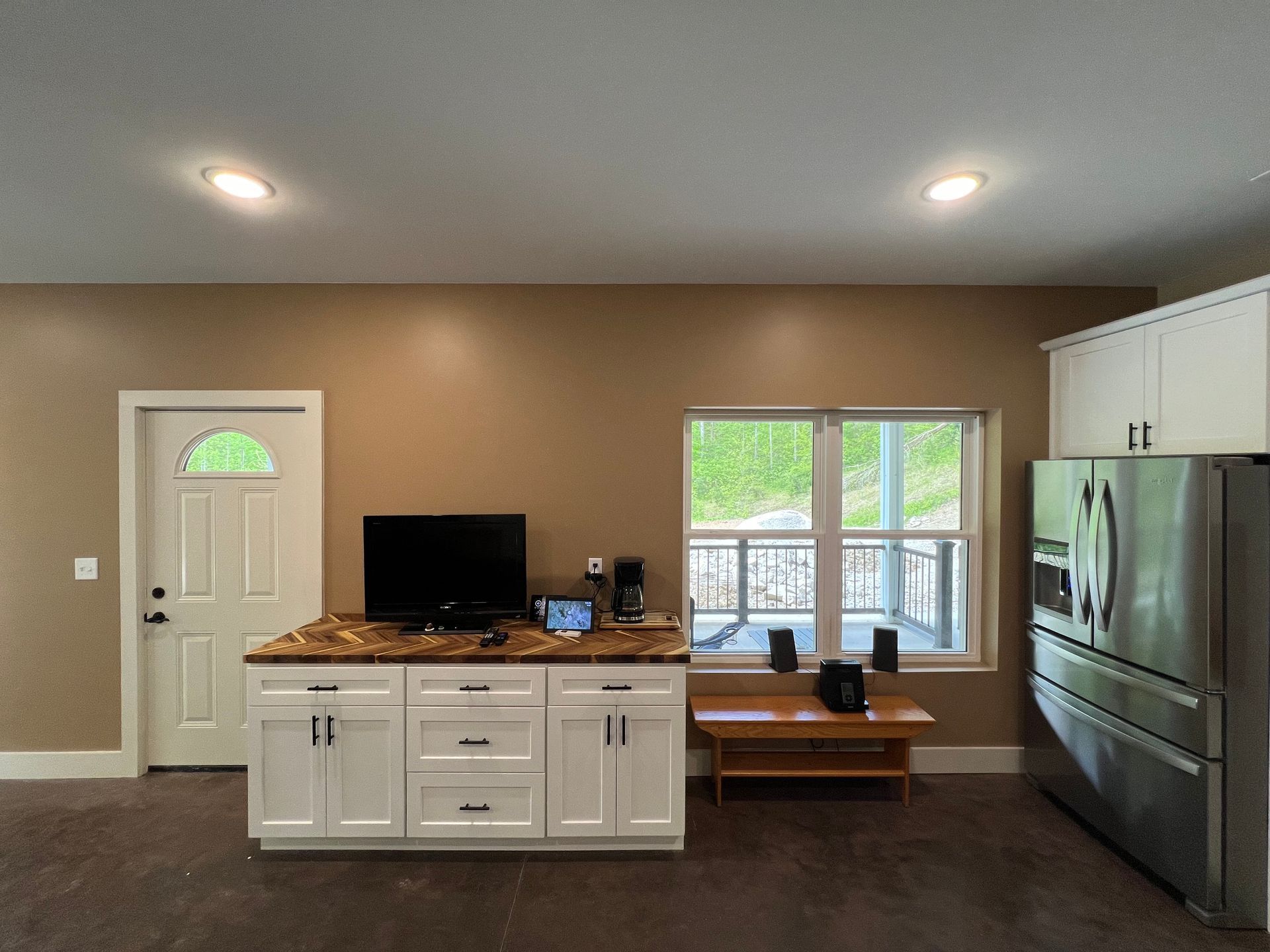 Kitchen with white cabinets, brown countertops, appliances, and a door and window with an outdoor view.