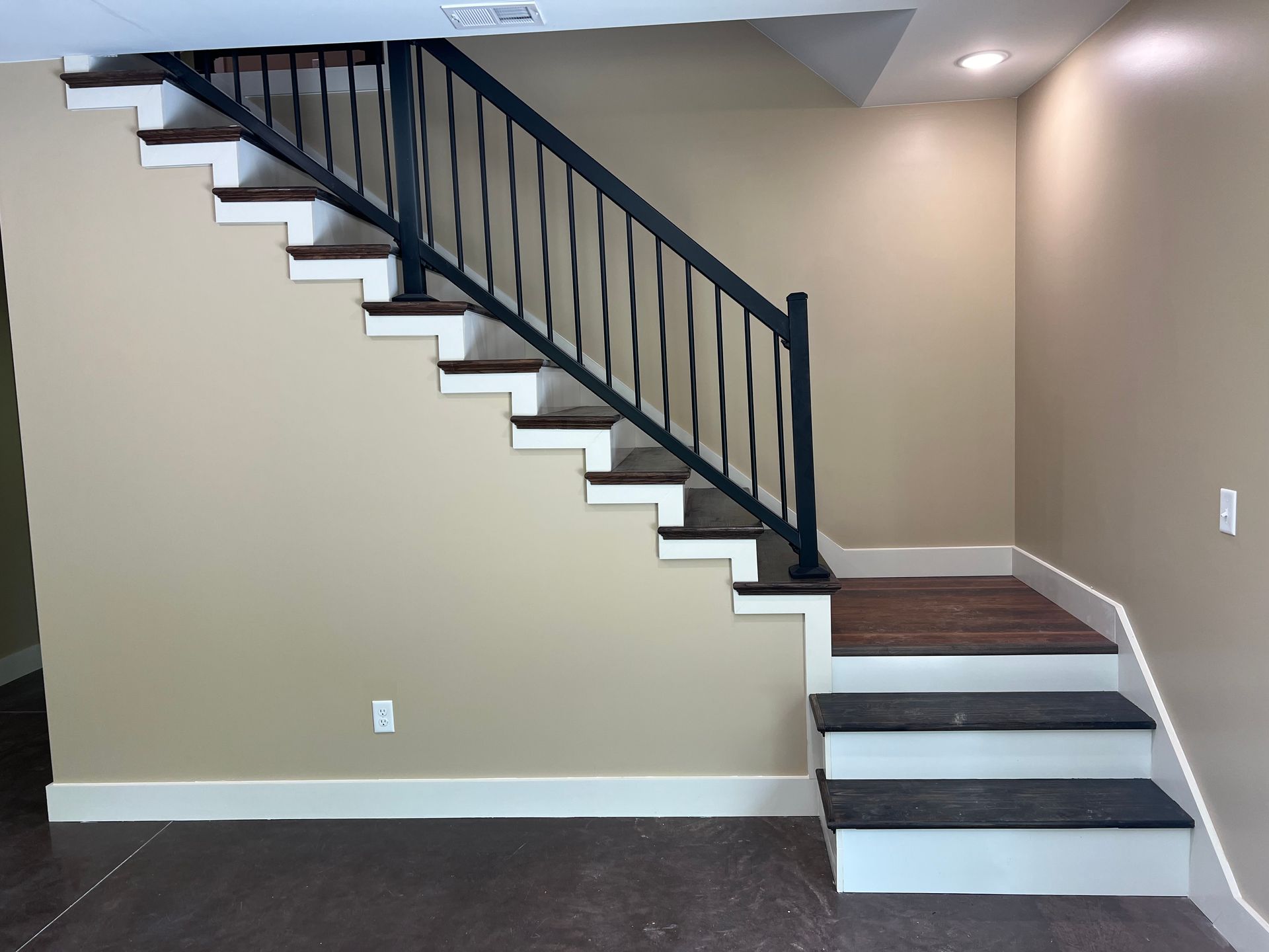 Staircase with dark wooden steps, white risers, and a black metal railing against a beige wall.