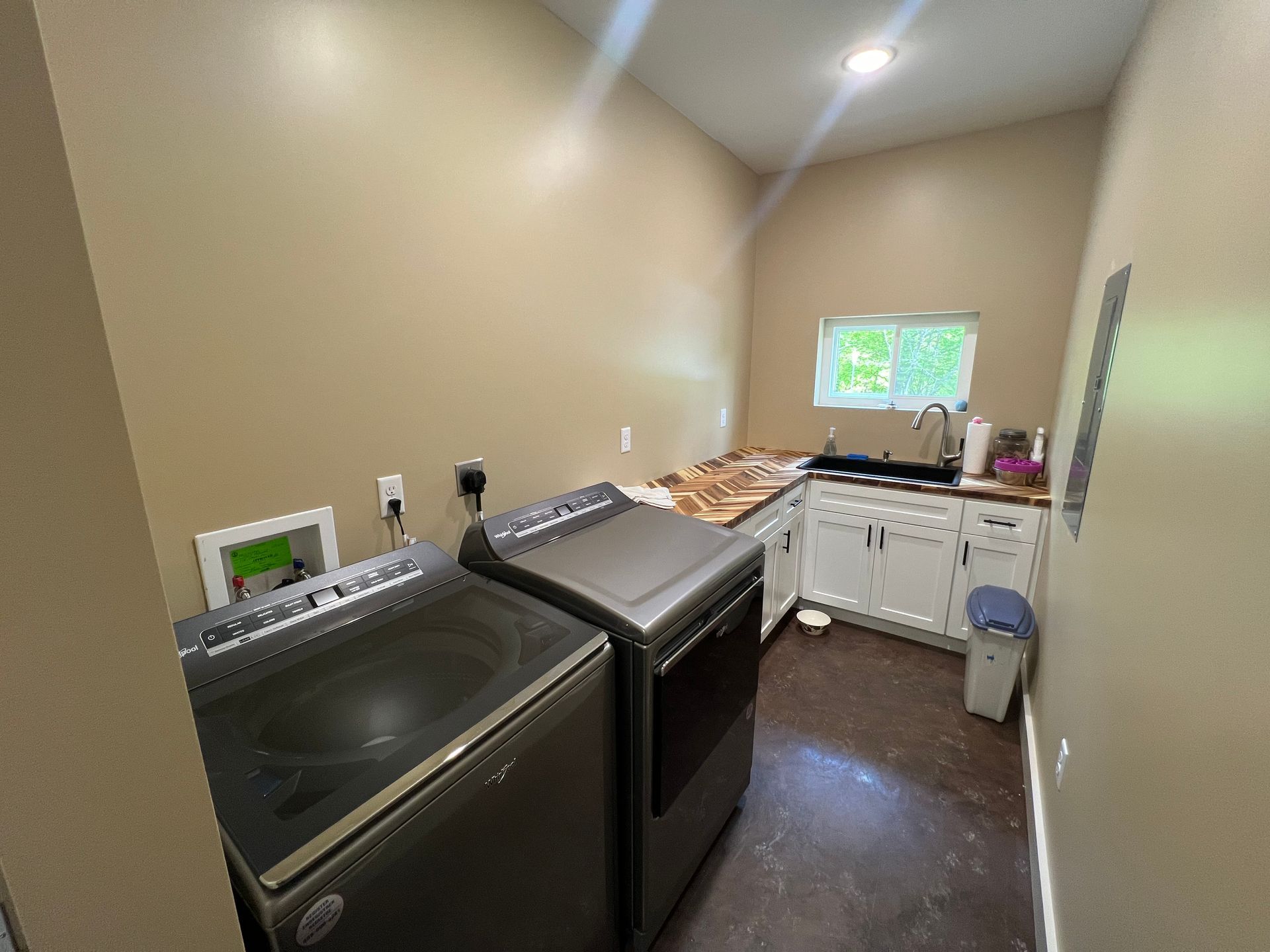 Laundry room with a washer and dryer, sink, and cabinets. The walls are beige and the floor is dark.