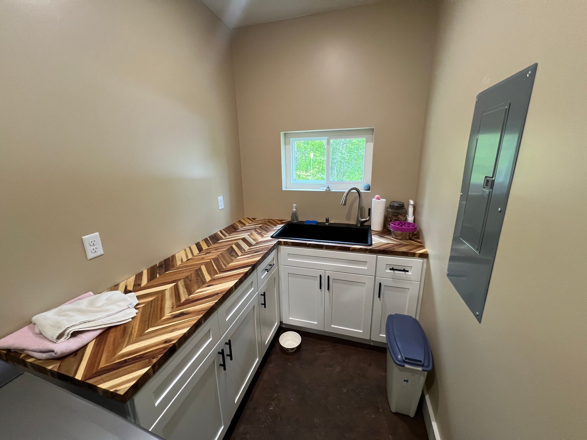 Laundry room with white cabinets, a wood countertop with a chevron pattern, a black sink, and a window.