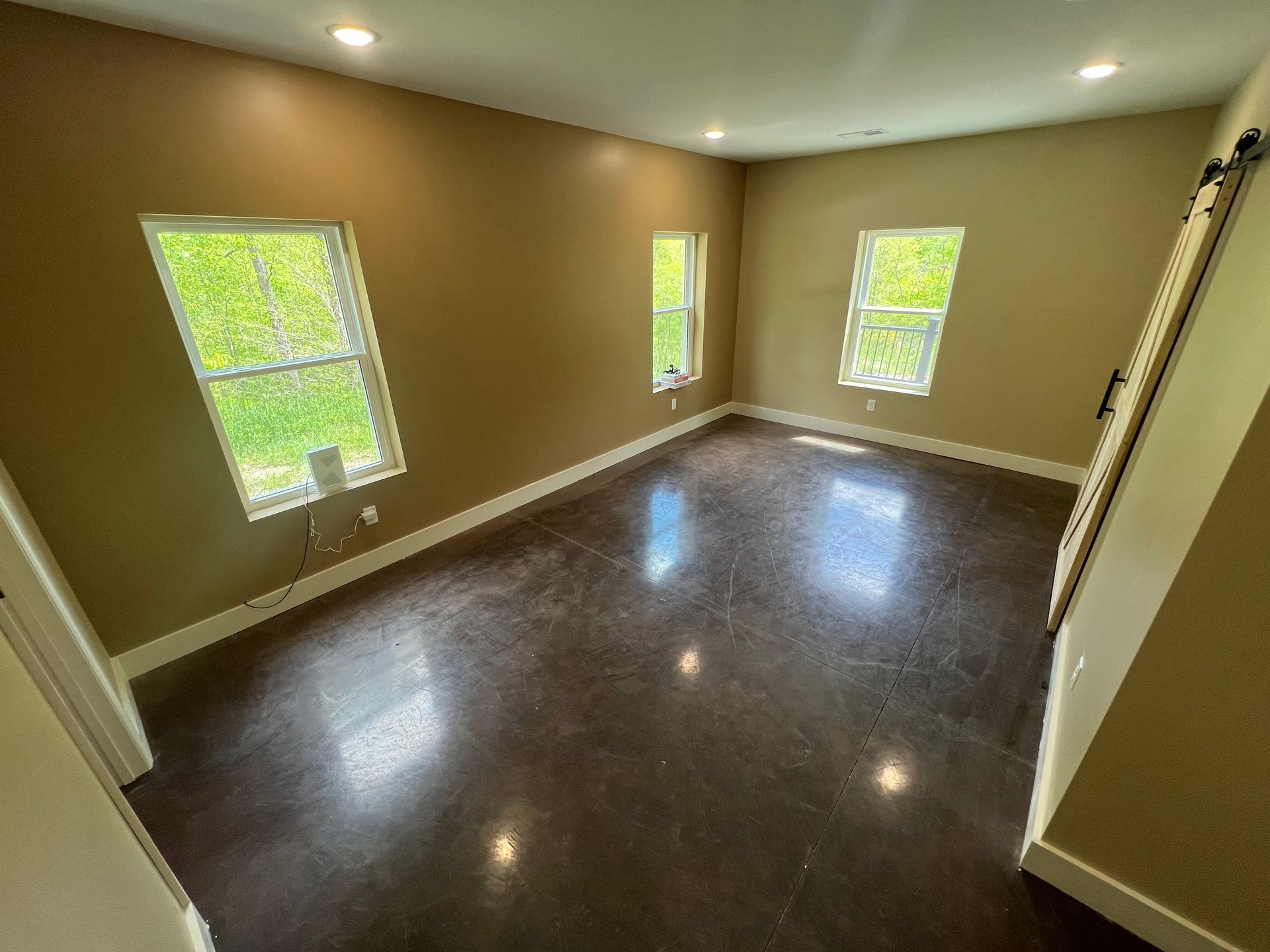 Empty room with brown walls and dark floor, three windows, and a sliding door.
