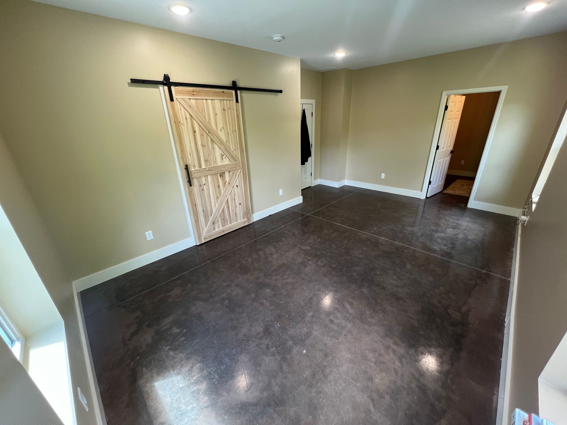Spacious room with stained concrete floor, a rustic sliding barn door, and two other doorways, painted walls.
