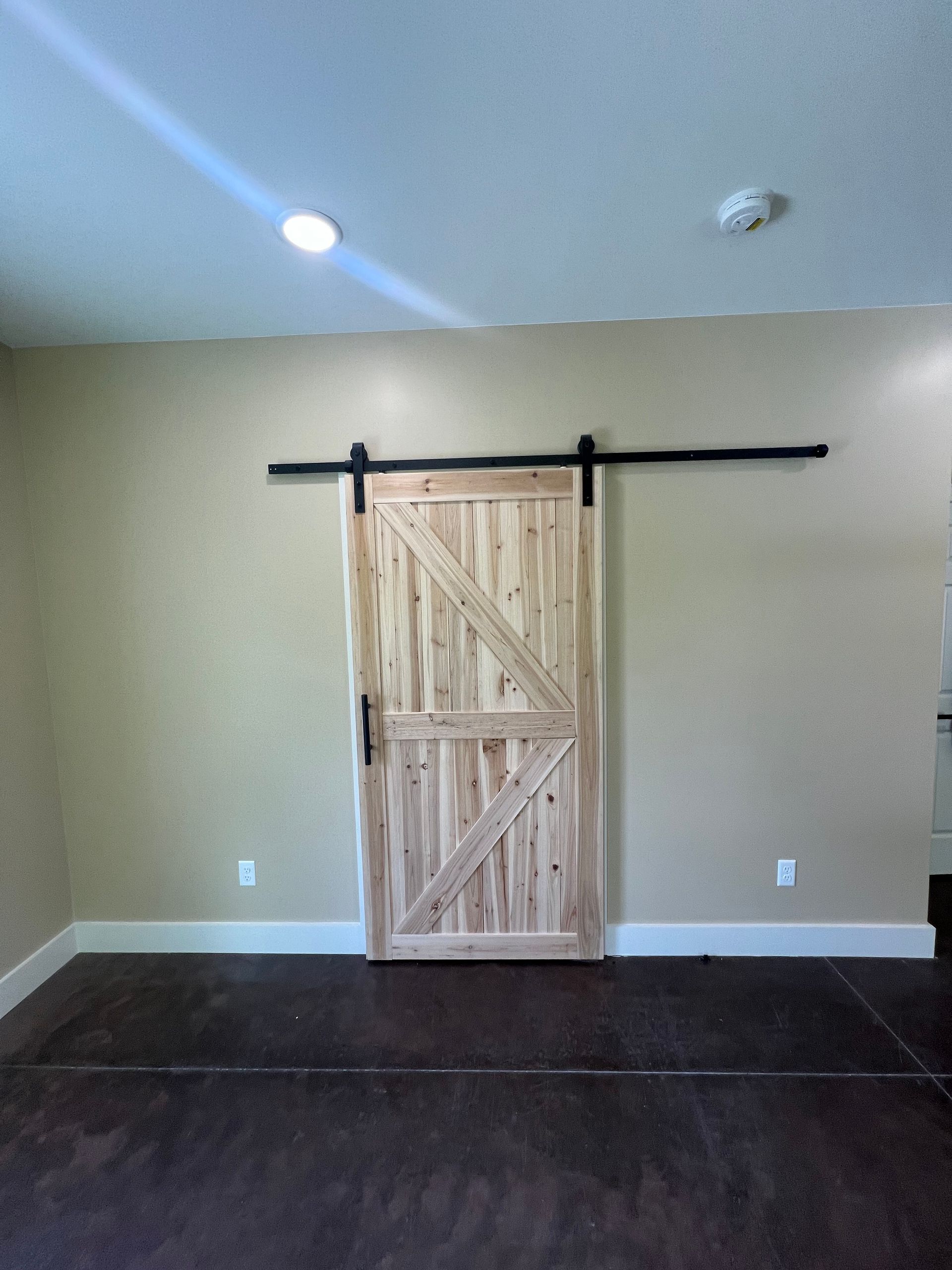 A rustic barn door on a black track in a room with beige walls and dark flooring.