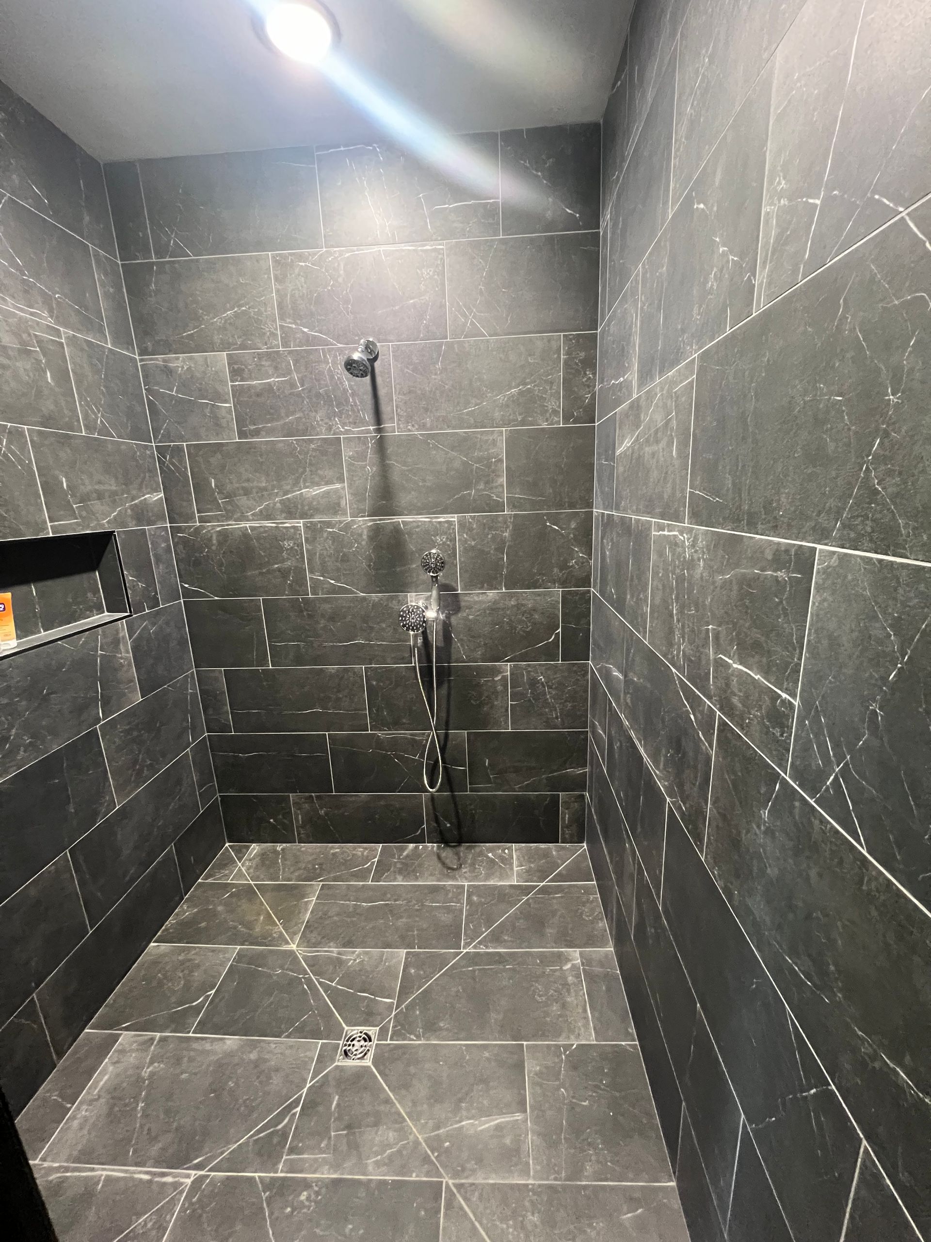 A dark, tiled shower with black walls and floor. A showerhead and fixtures are visible.