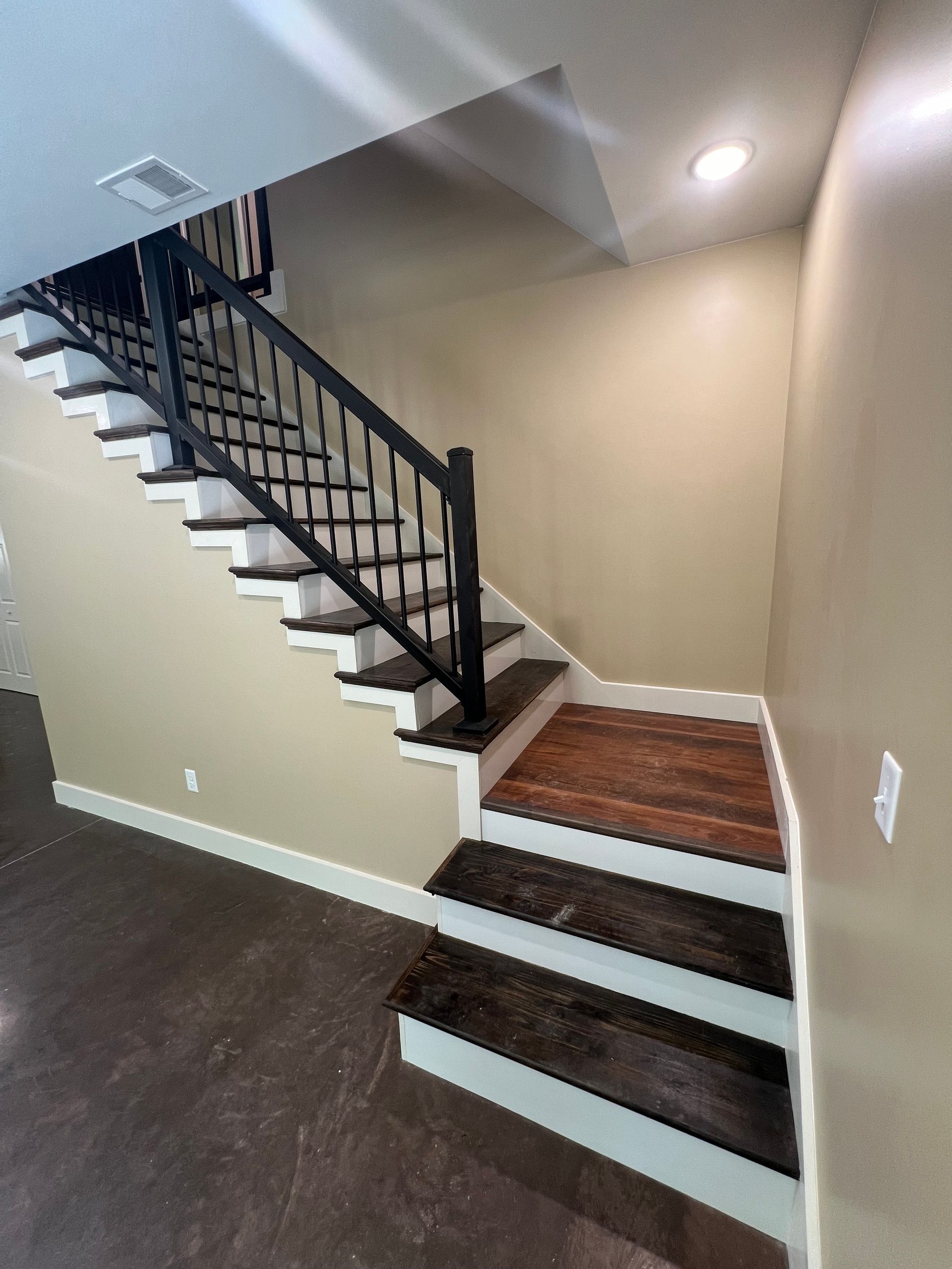 Staircase with black banister and white risers against beige walls. The steps are dark brown.