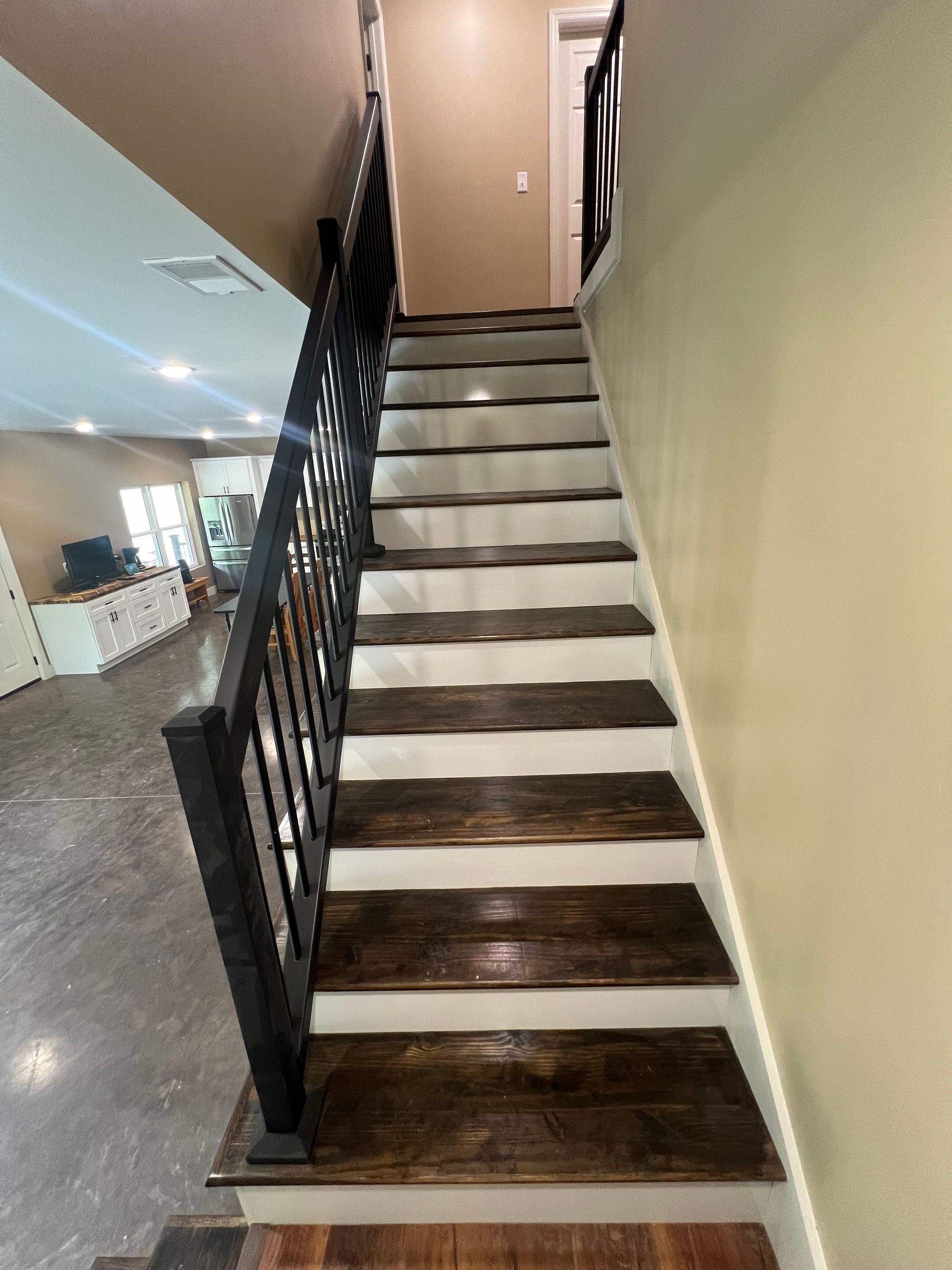Wooden staircase with dark brown treads and white risers, black handrails. The staircase leads upwards, with a view of a door at the top.