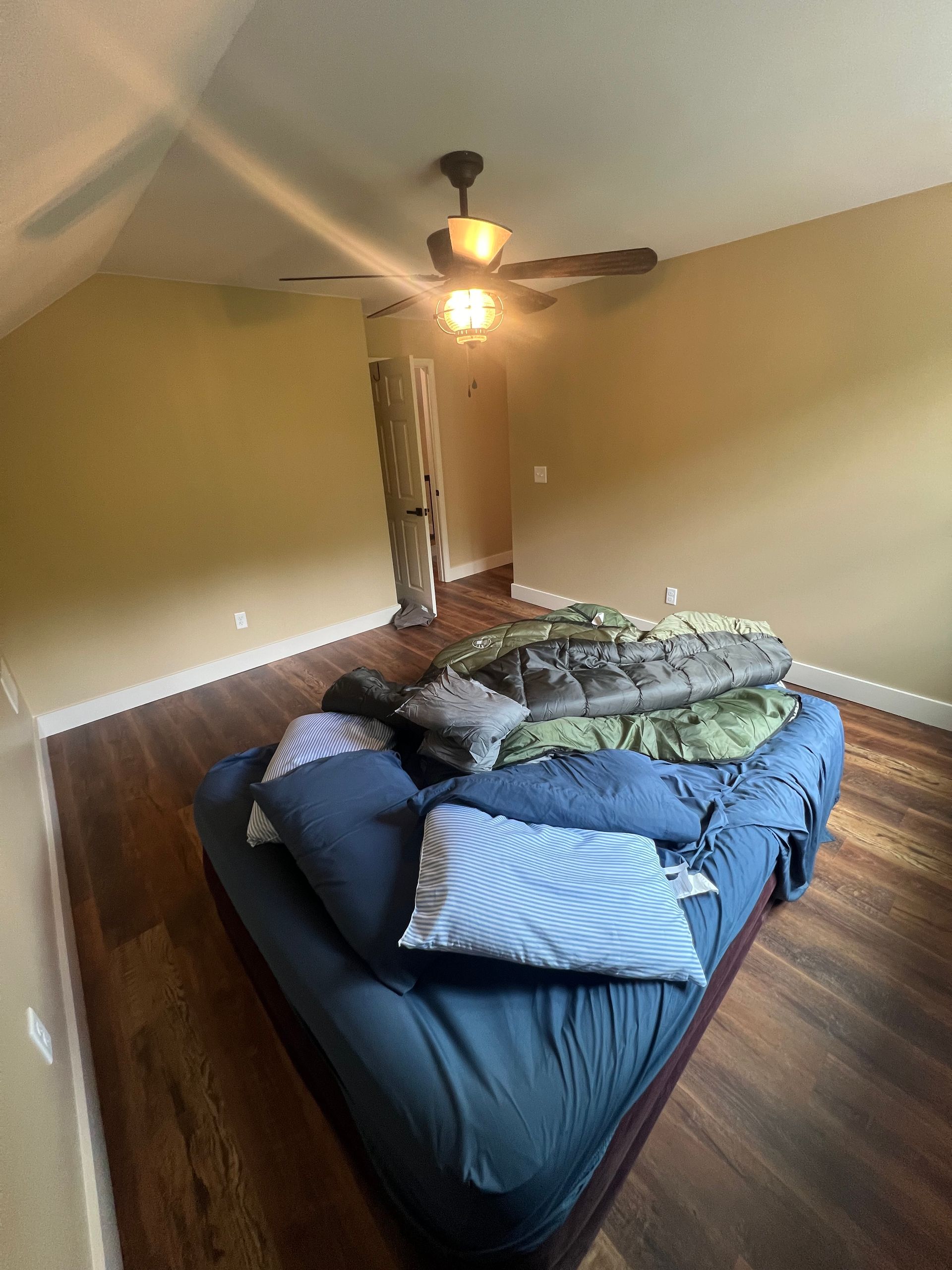 Bedroom with a bed covered in blankets and pillows; hardwood floors and a ceiling fan.