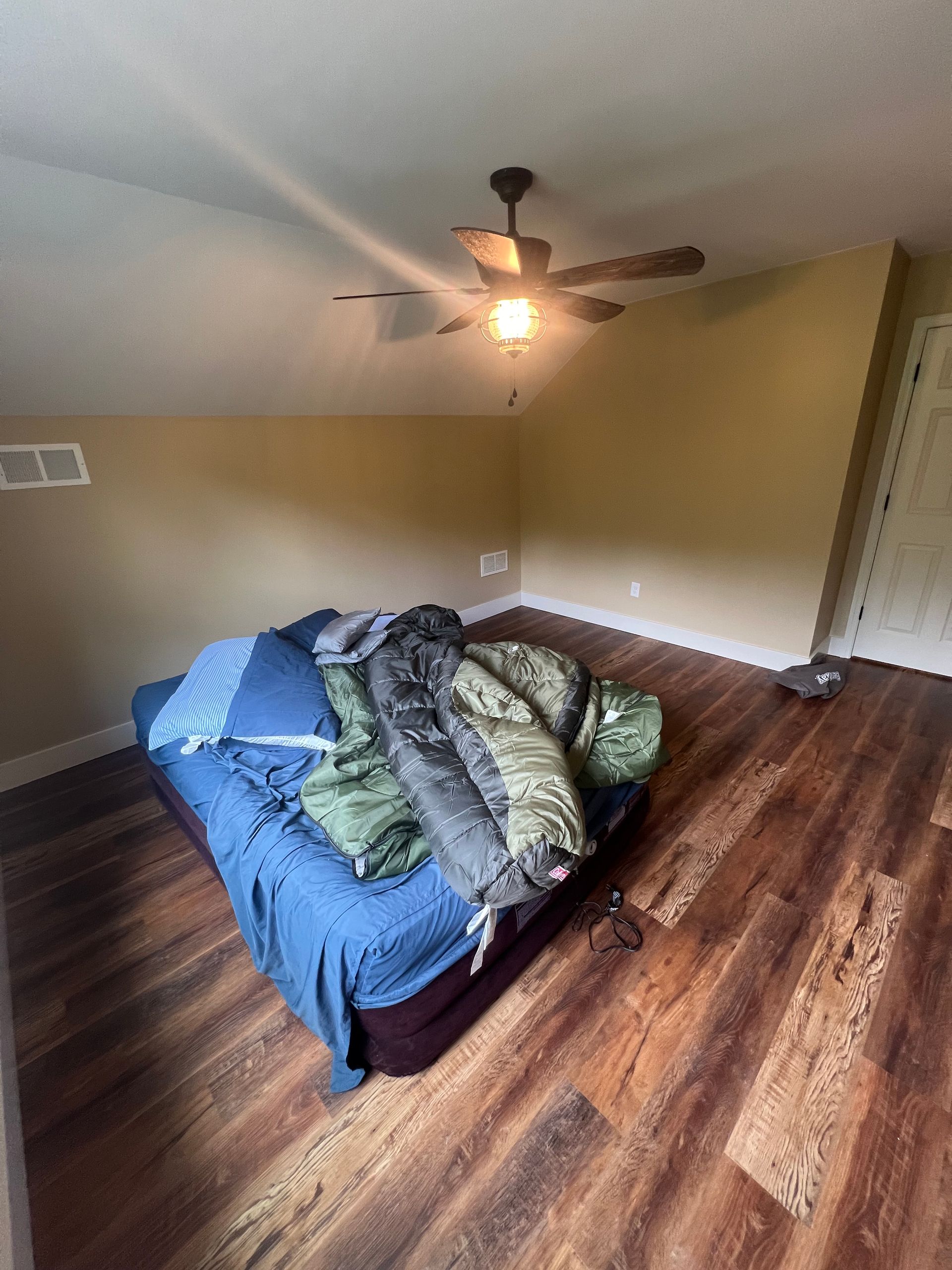 Bedroom with unmade bed, hardwood floors, and ceiling fan; walls are beige.