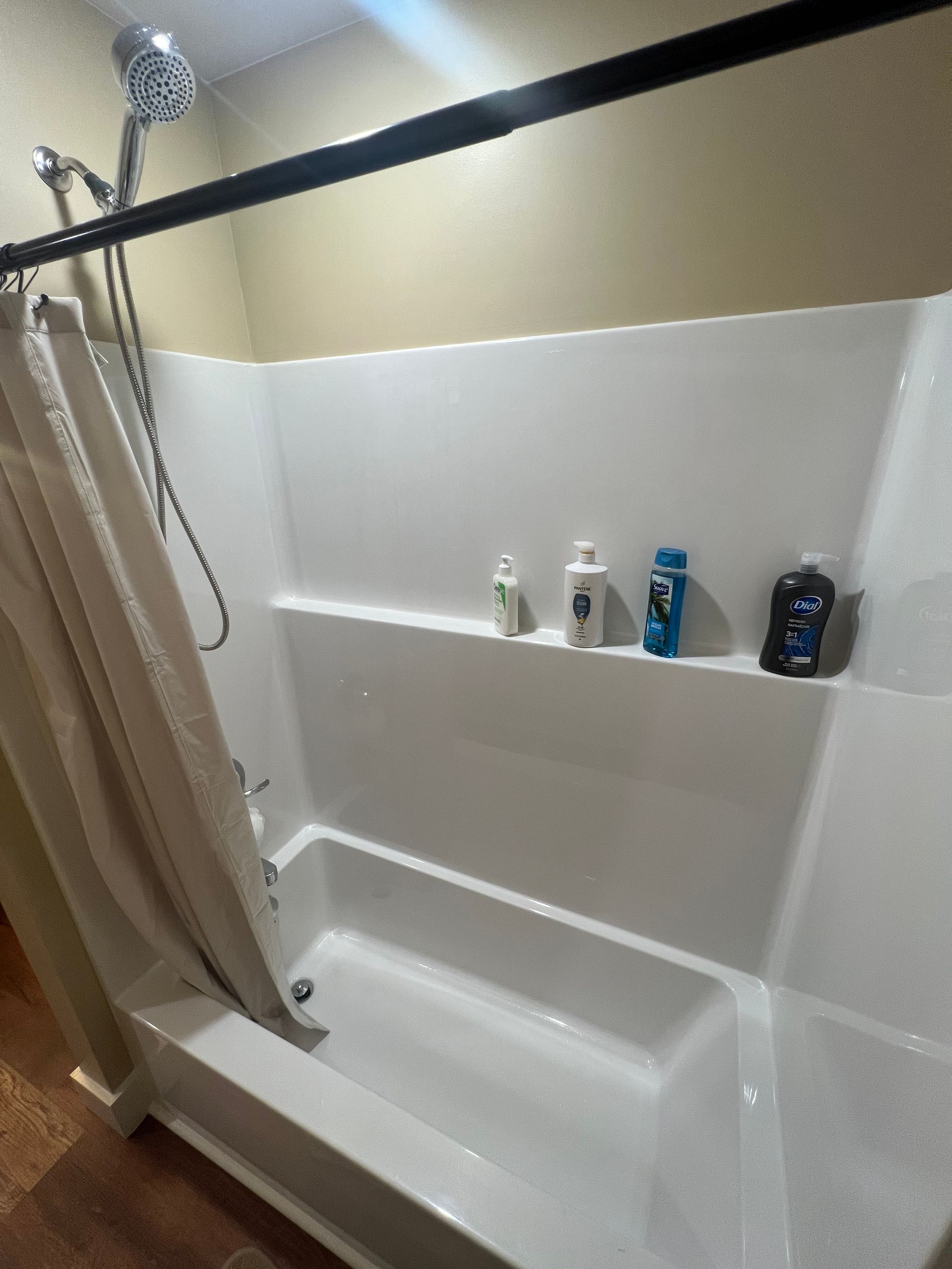 A white shower with a shelf holding toiletries, a shower curtain, and a silver showerhead.