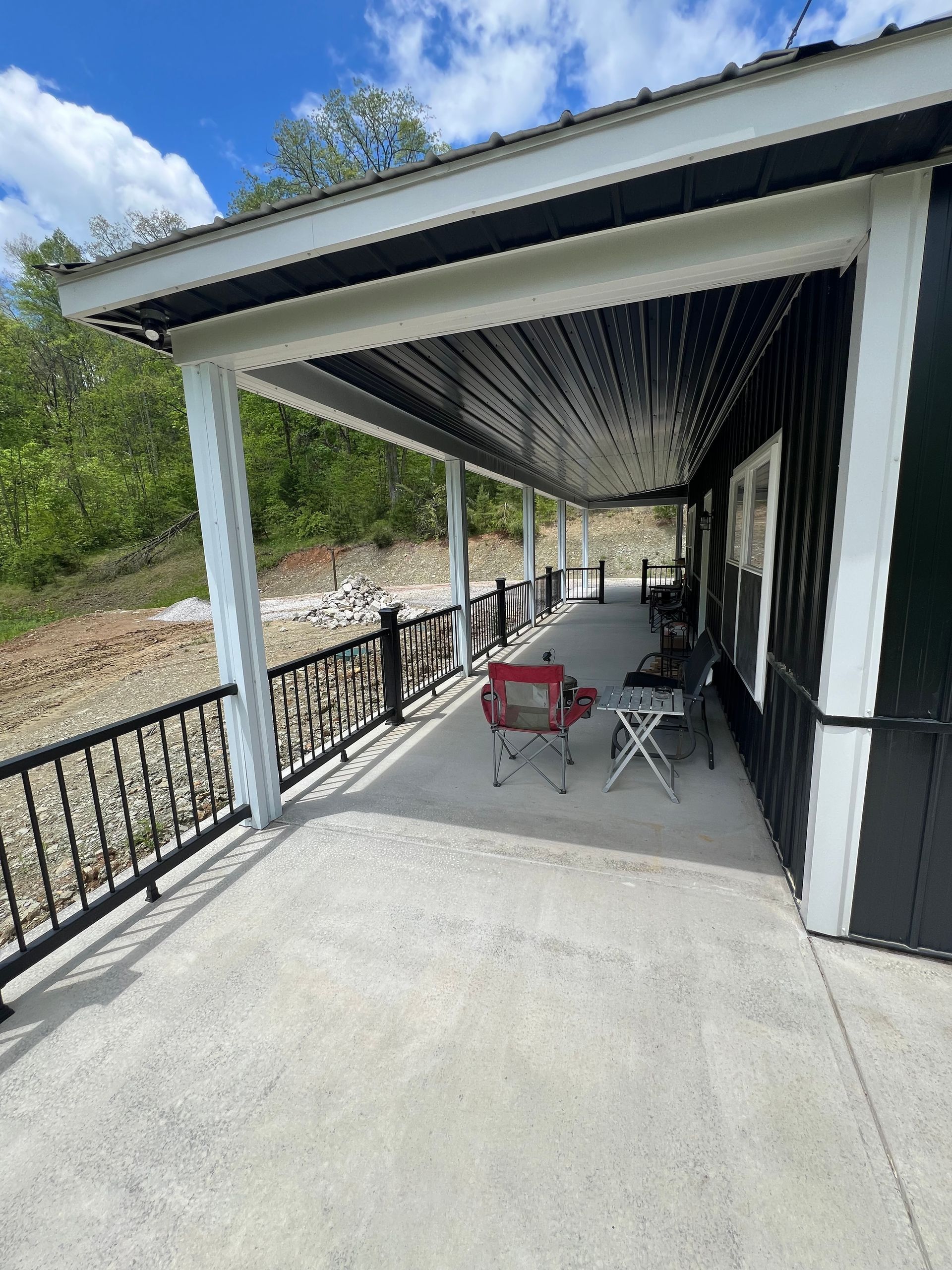 A black cabin with a long porch under a white roof, with black railings, and a concrete floor.