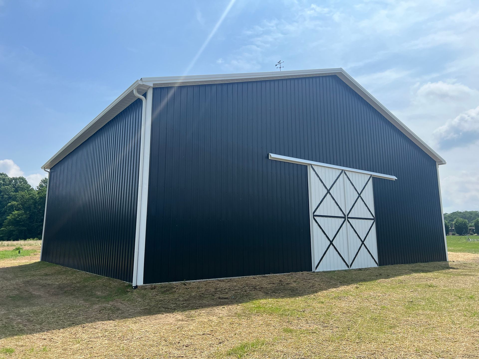 Black metal barn with white trim and sliding door, set in a field under a blue sky.