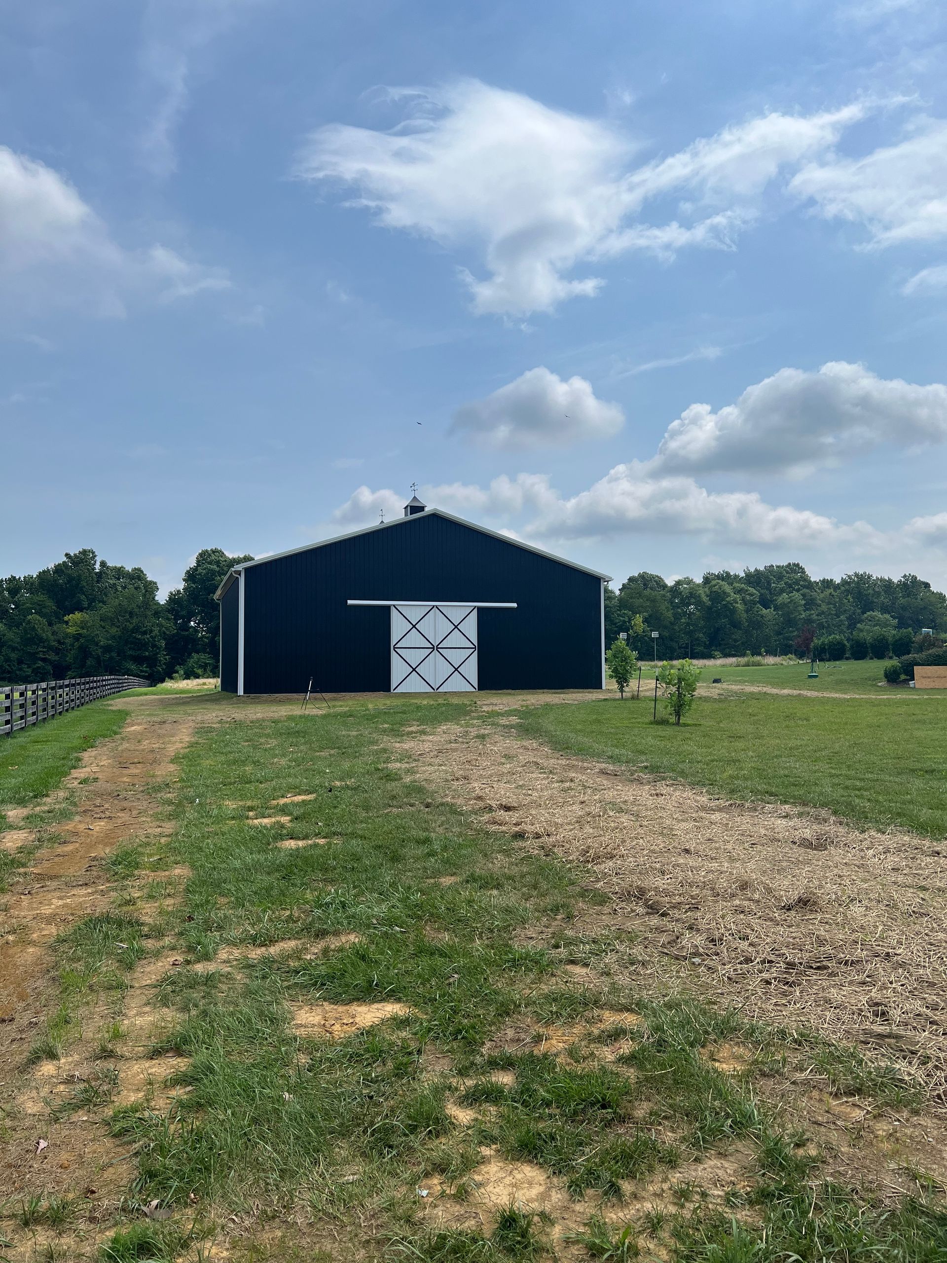 A dark blue barn with white doors stands in a grassy field under a partly cloudy sky.