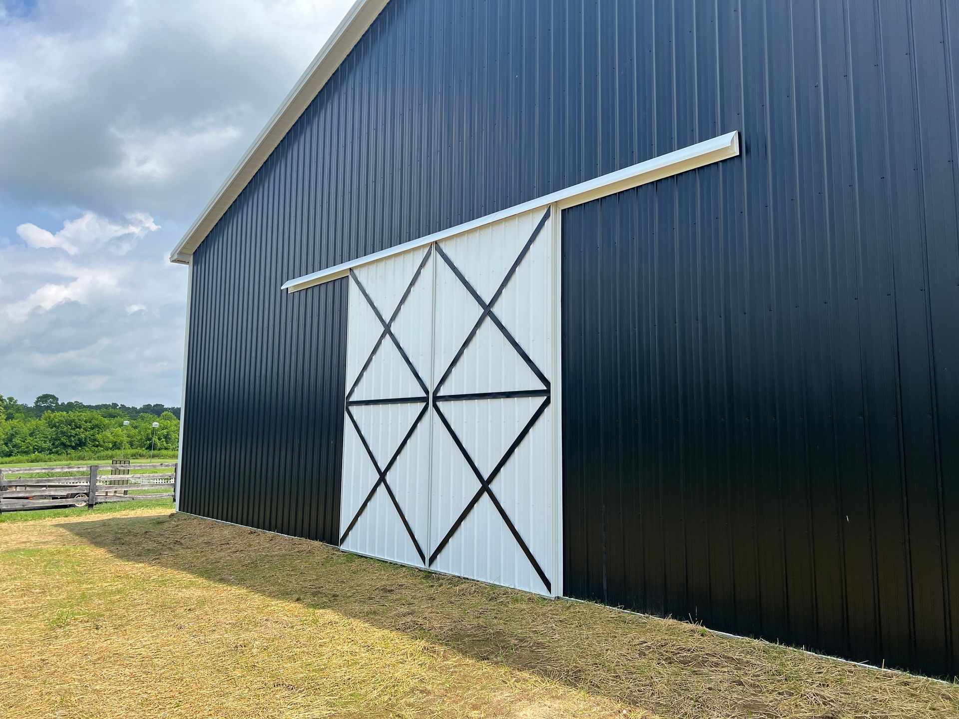 Black metal barn with a large white sliding door. The door has black cross-bracing.