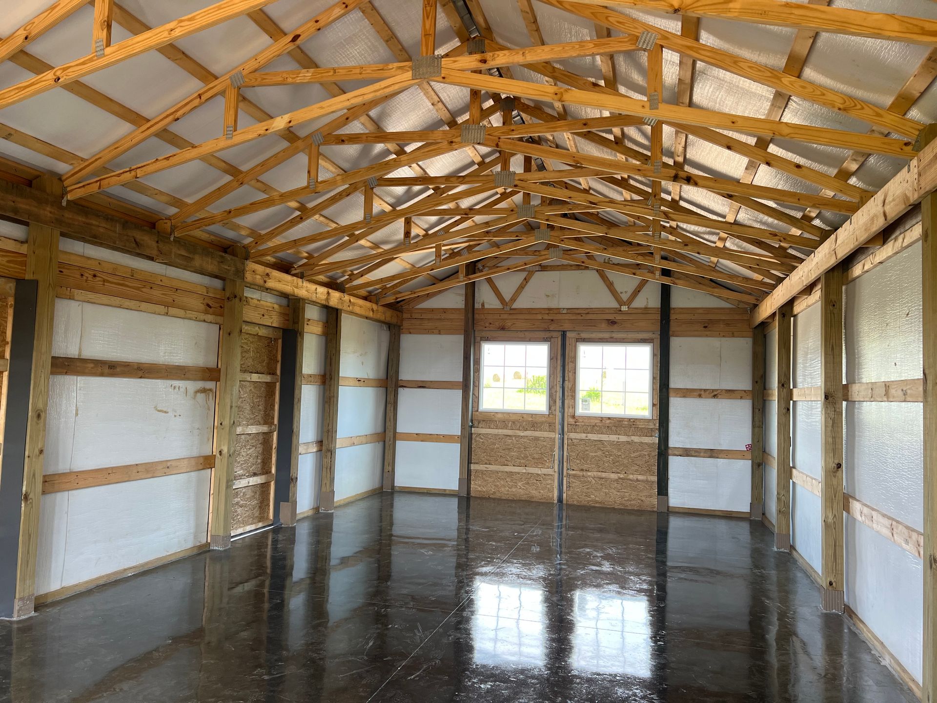 Interior view of a newly built wooden building with a concrete floor. Framing is visible, with potential for insulation on the walls.