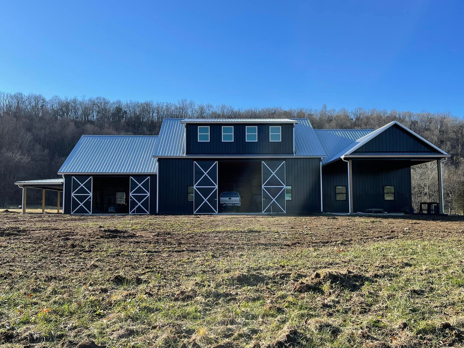 A dark blue barn-style house with a metal roof and white accents, set in a rural field with trees in the background.