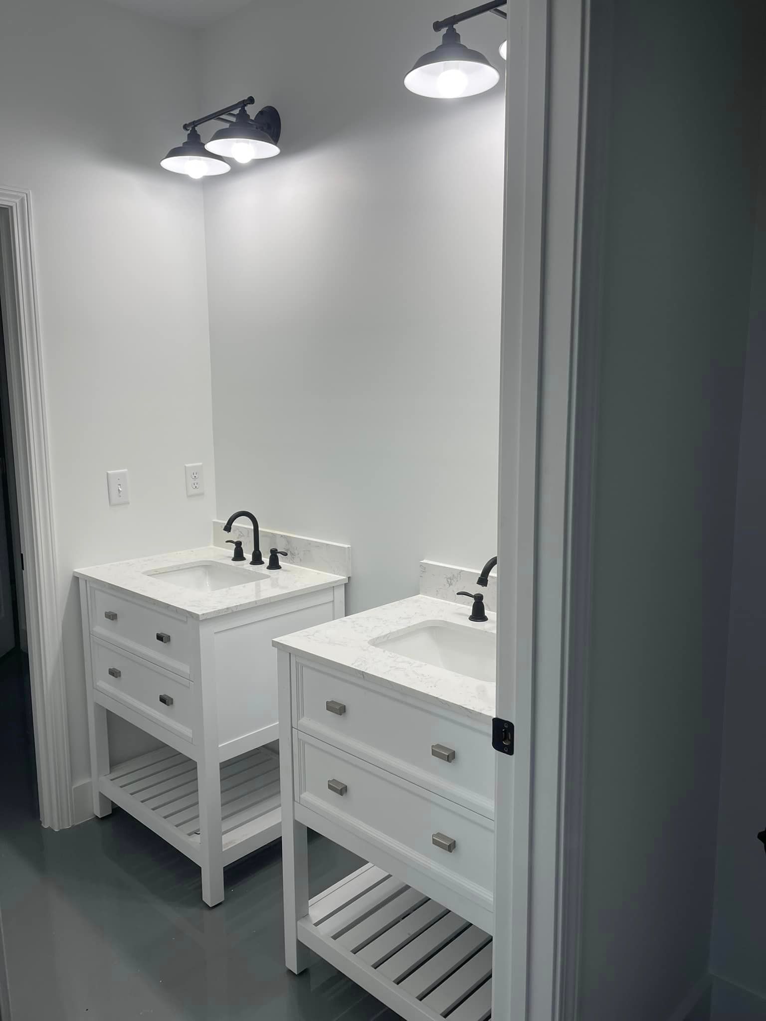 Two white bathroom vanities with sinks and black fixtures, each with a white countertop and a light fixture above.
