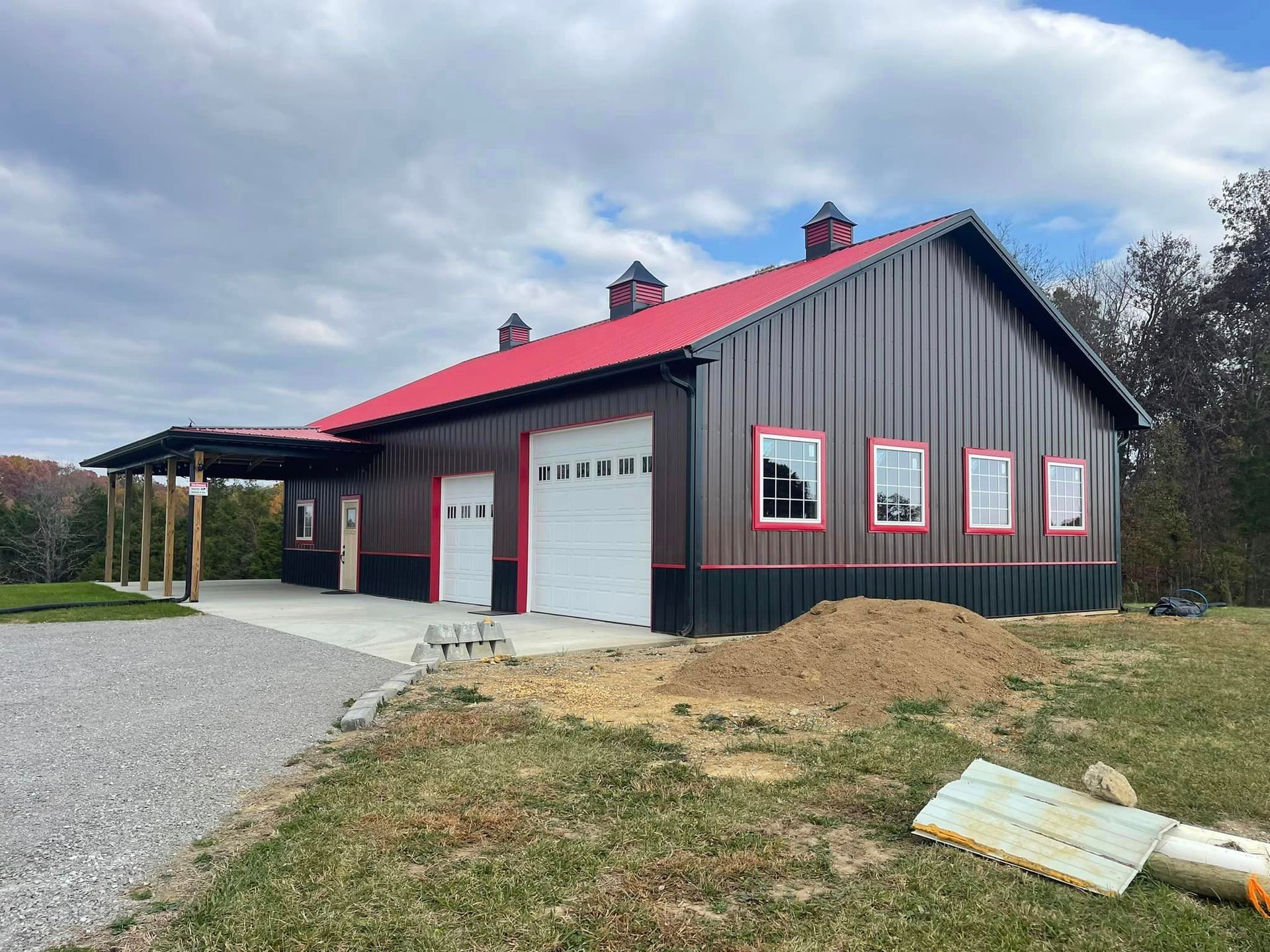 Dark gray barn with red trim and roof, white garage doors and windows, and a covered porch on a cloudy day.