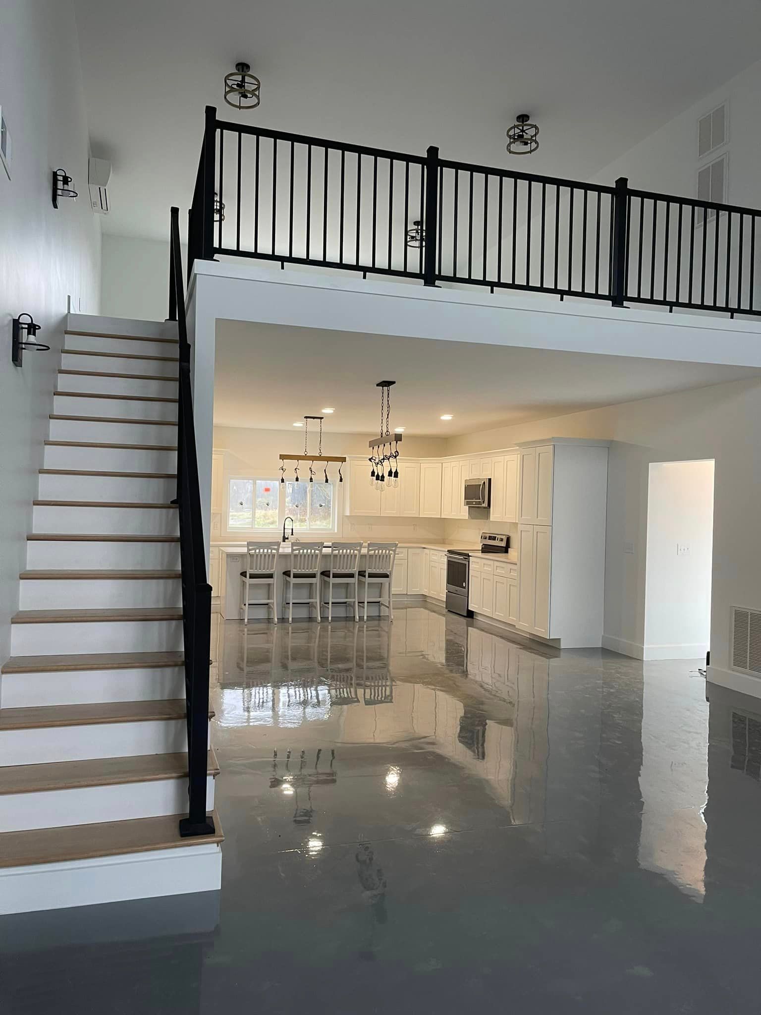 Interior view of a modern home with a loft, featuring white walls, stairs, a kitchen with a bar, and a polished gray floor.