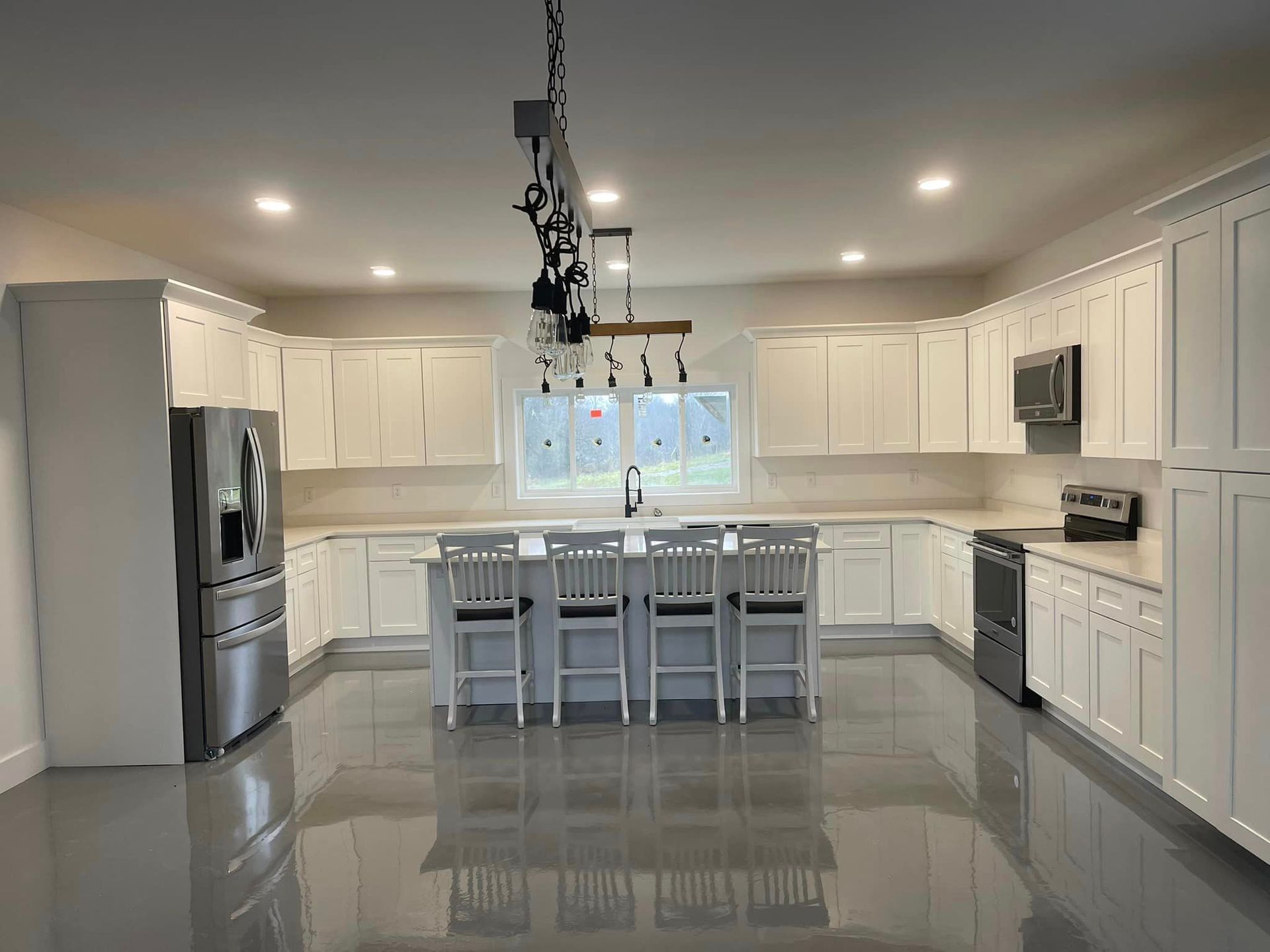 Bright, spacious kitchen with white cabinets, stainless steel appliances, a center island, and gray flooring.