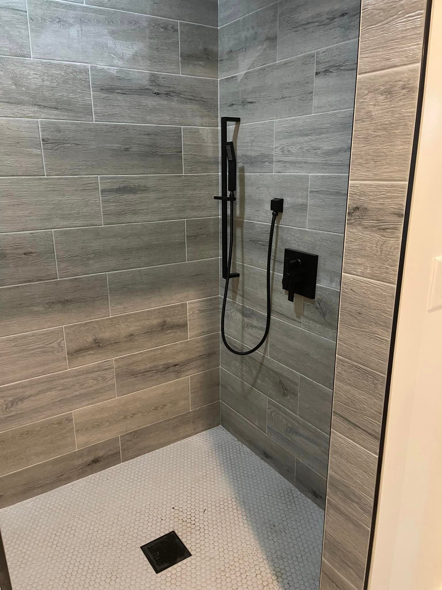Modern shower with gray tile walls, white tile floor, and black shower fixtures.