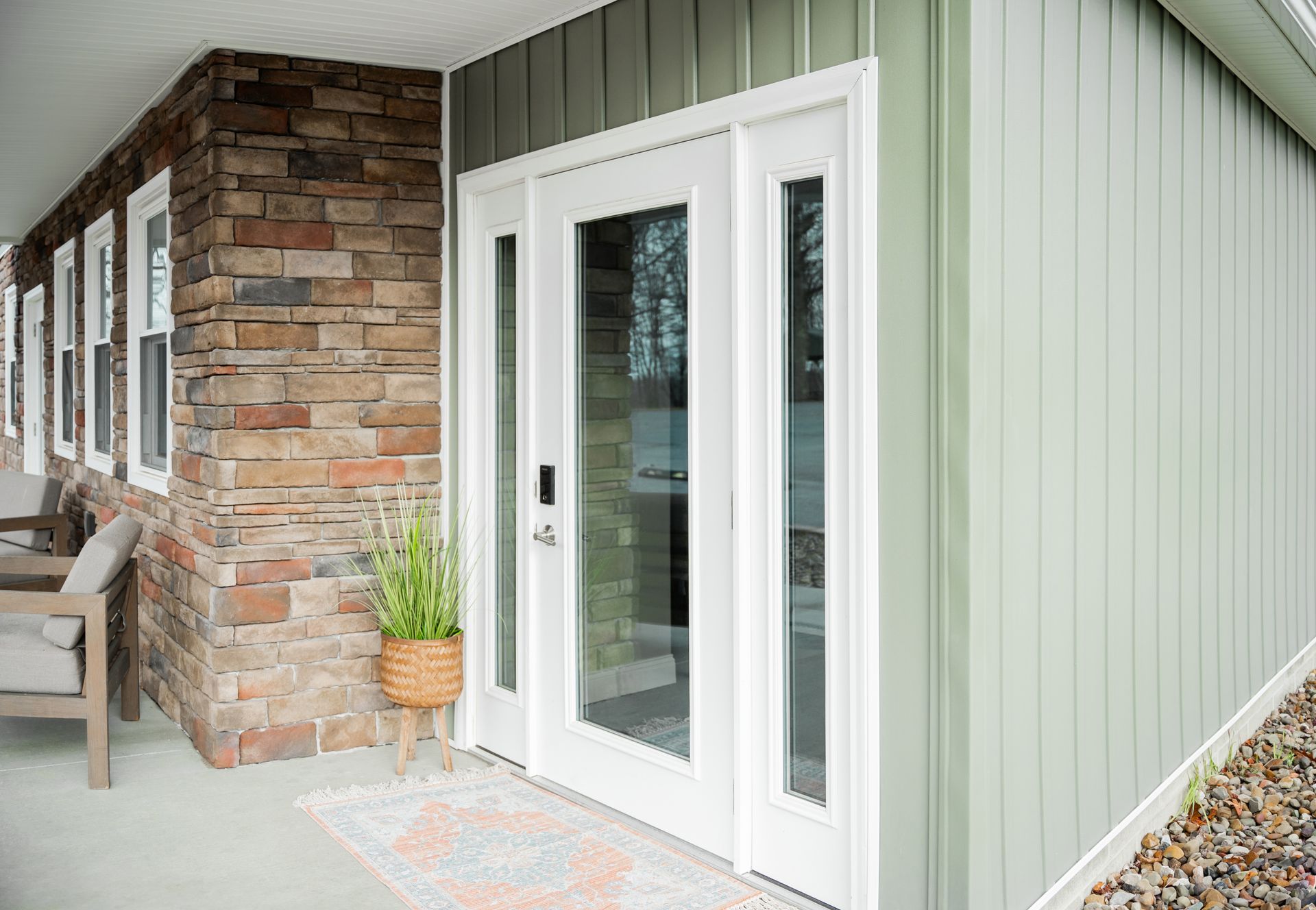 Exterior of a house with a white double door and glass side panels. The wall is stone on the left and green siding on the right.