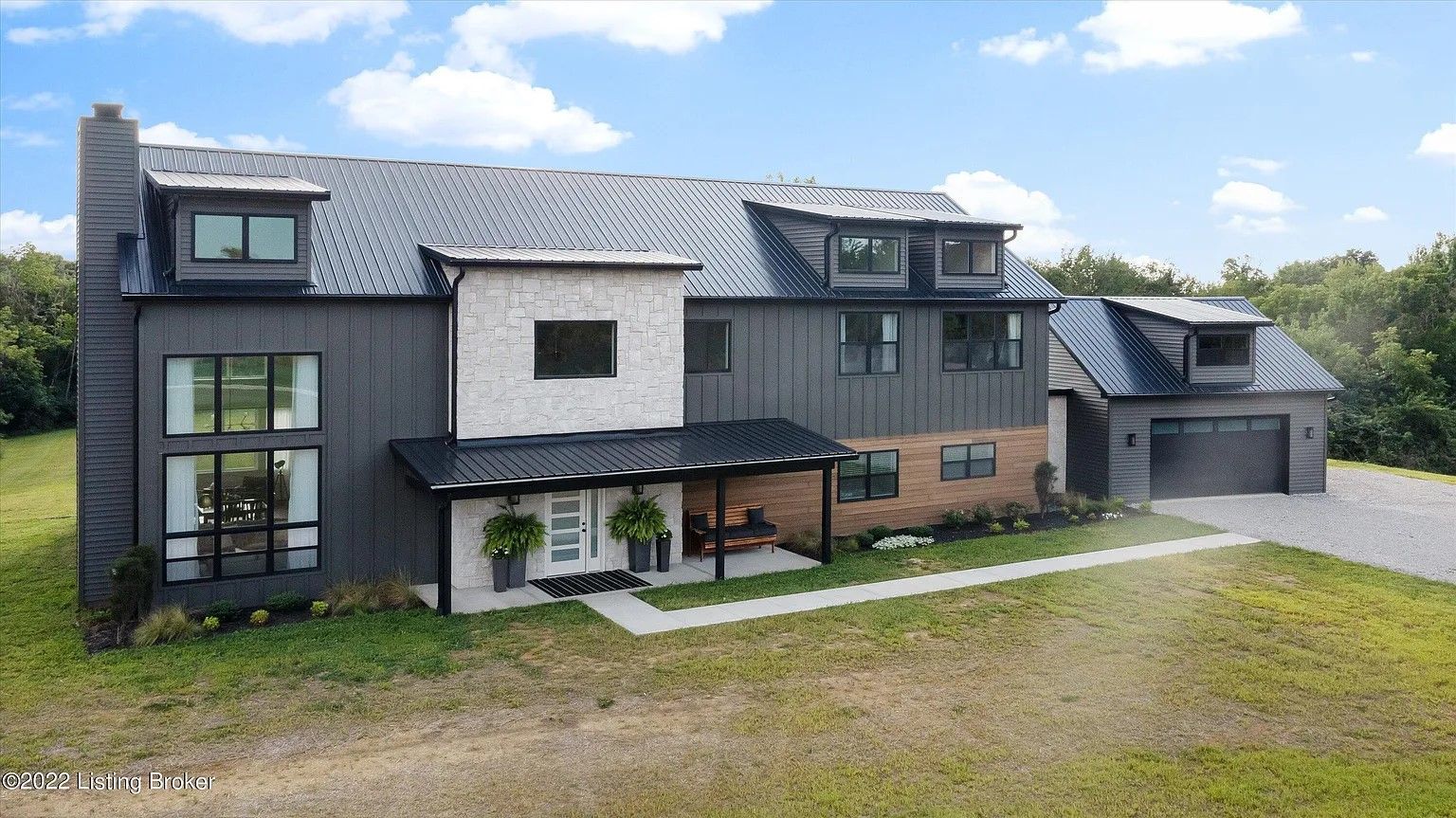 Modern two-story house with dark gray siding, a white brick section, and a detached garage. The house is on a grassy lot with a paved walkway.