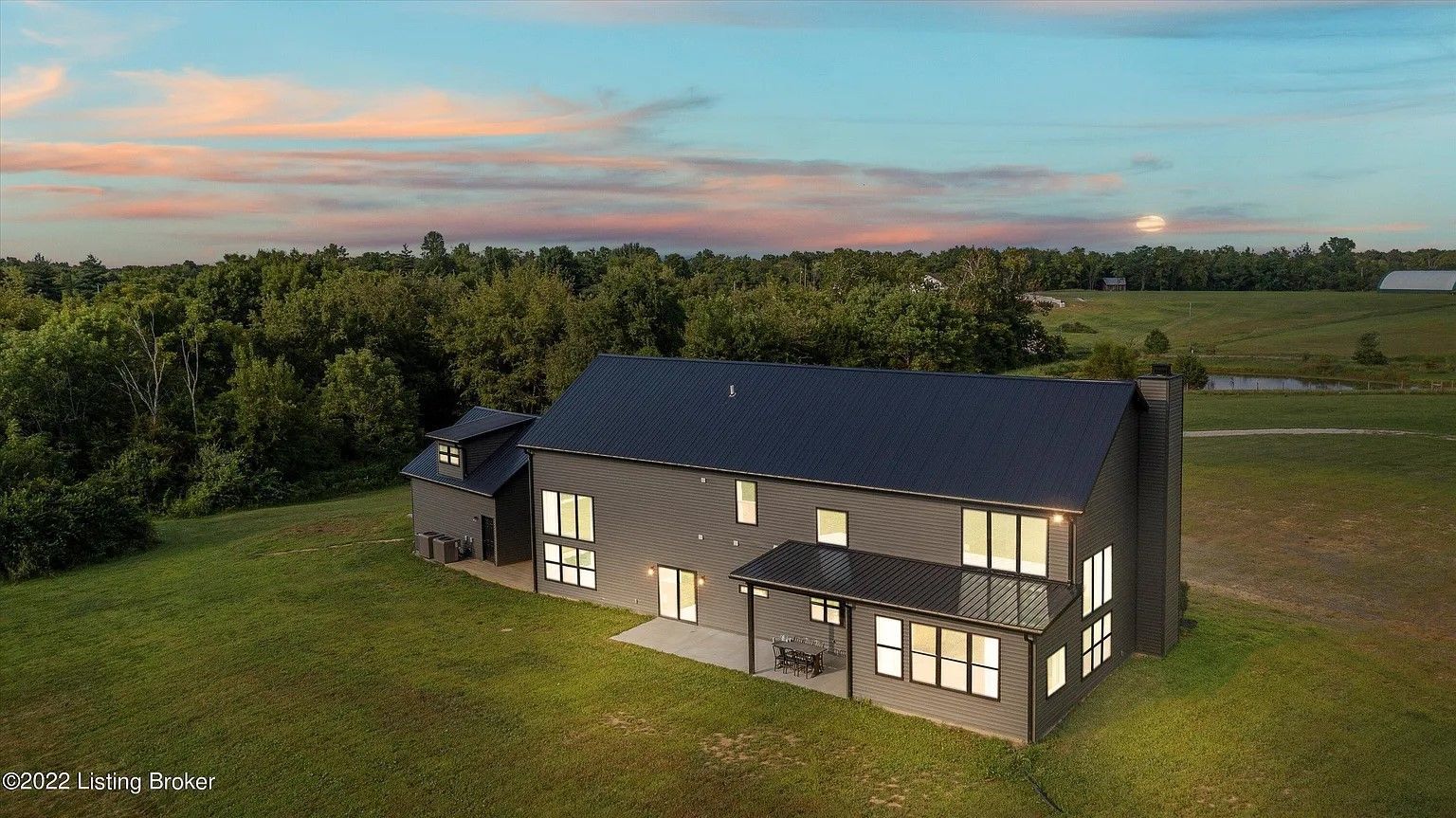Modern two-story house at dusk. Gray siding, large windows, and a dark roof stand out against the twilight sky and surrounding trees.