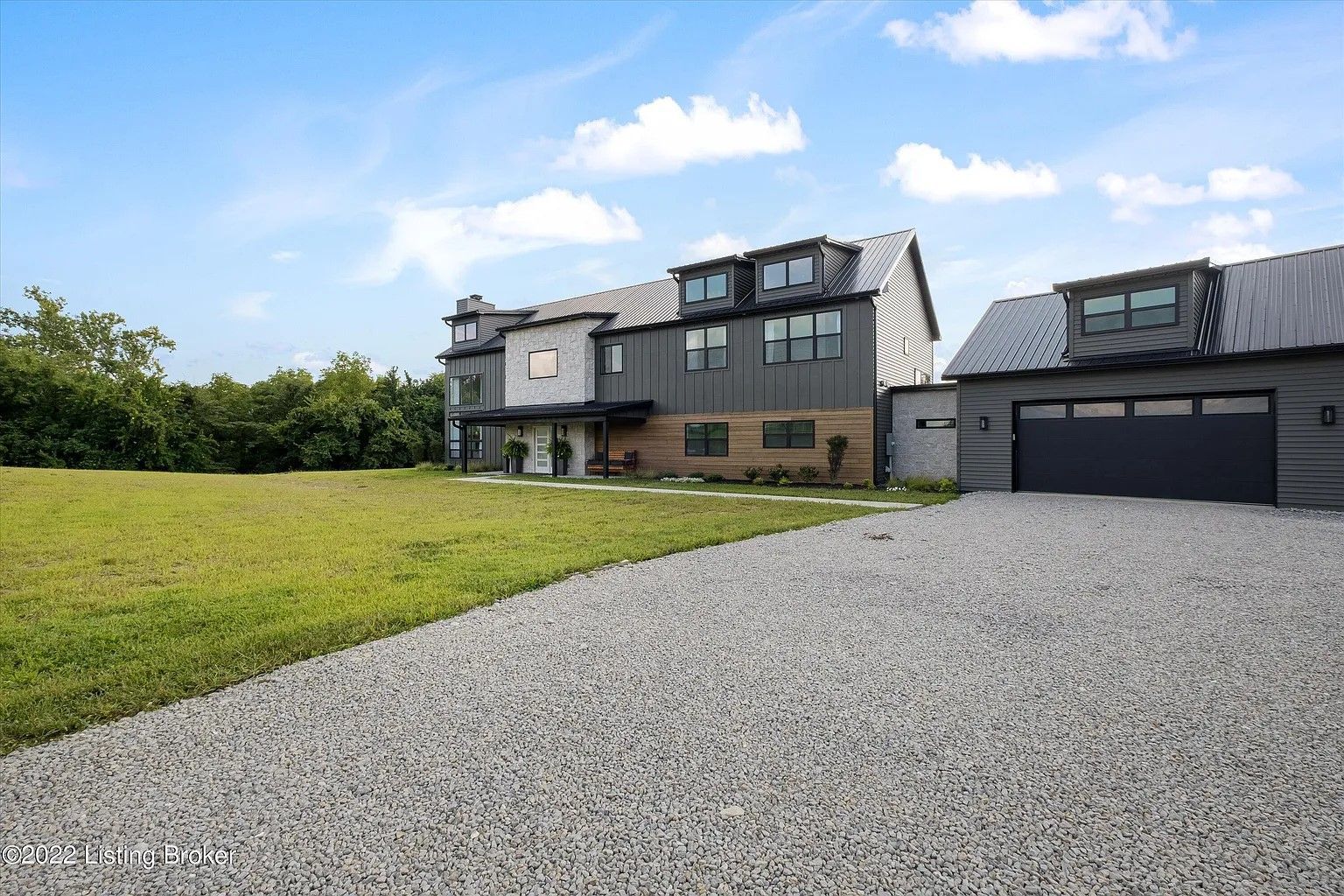 Modern two-story house with a gravel driveway, surrounded by green grass under a blue sky.