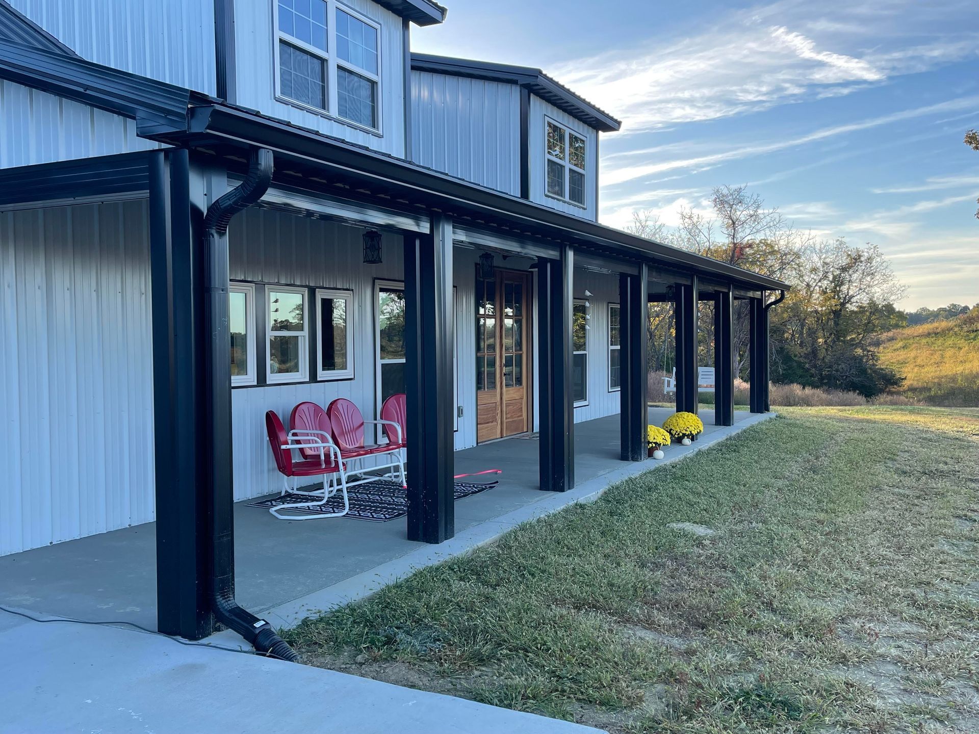 A white house with a black-columned porch. Two red rocking chairs sit on the porch. Green grass and a blue sky are in the background.