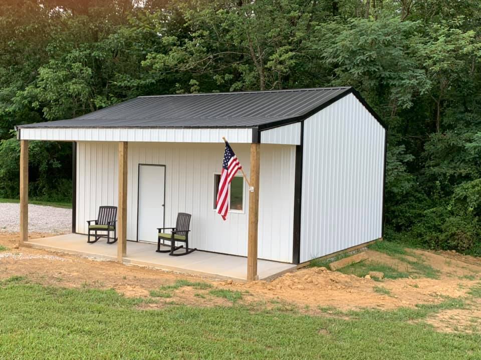 White metal building with a porch, black roof, and American flag. Two rocking chairs sit on the porch.
