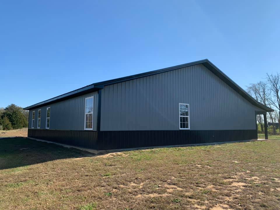 A dark gray and black metal building with windows, set against a clear blue sky and a grassy field.