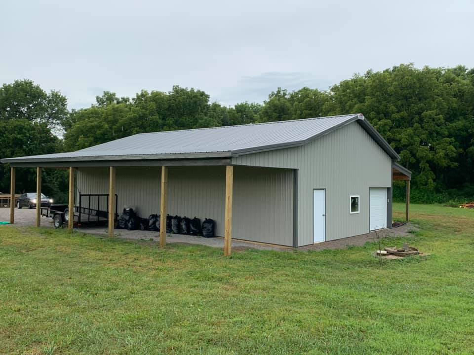 Green metal shed with a covered porch. The shed has a gray roof and light green siding, with a grassy yard in front.