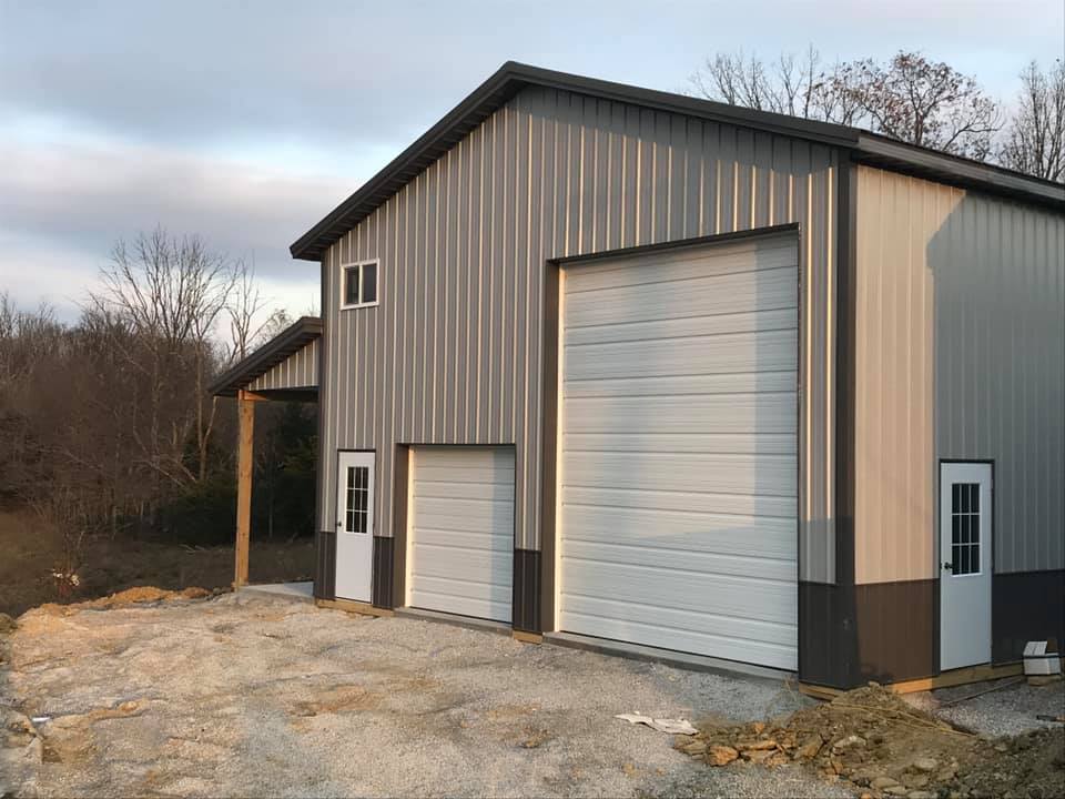 Gray and black metal barn with two garage doors and two white doors, set in a rural area with bare trees.