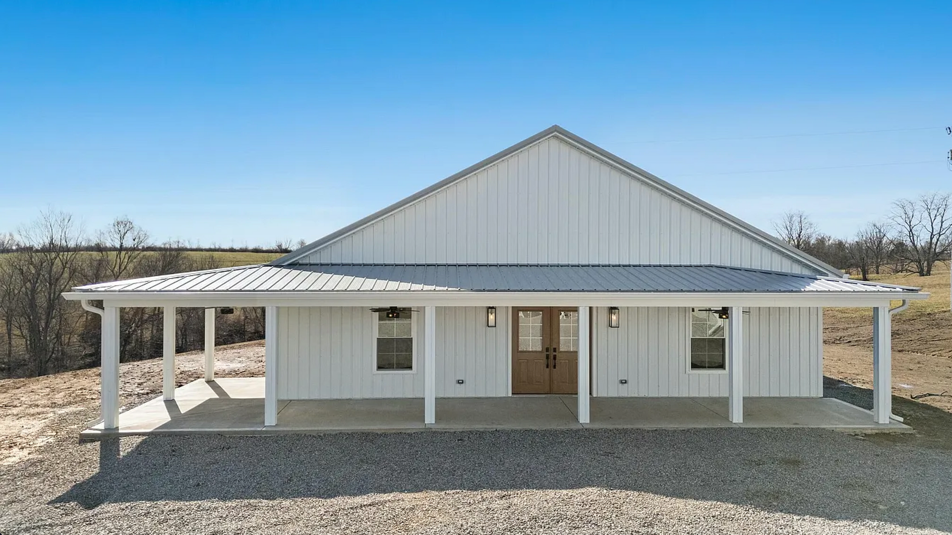 White farmhouse with a metal roof and covered porch against a blue sky.