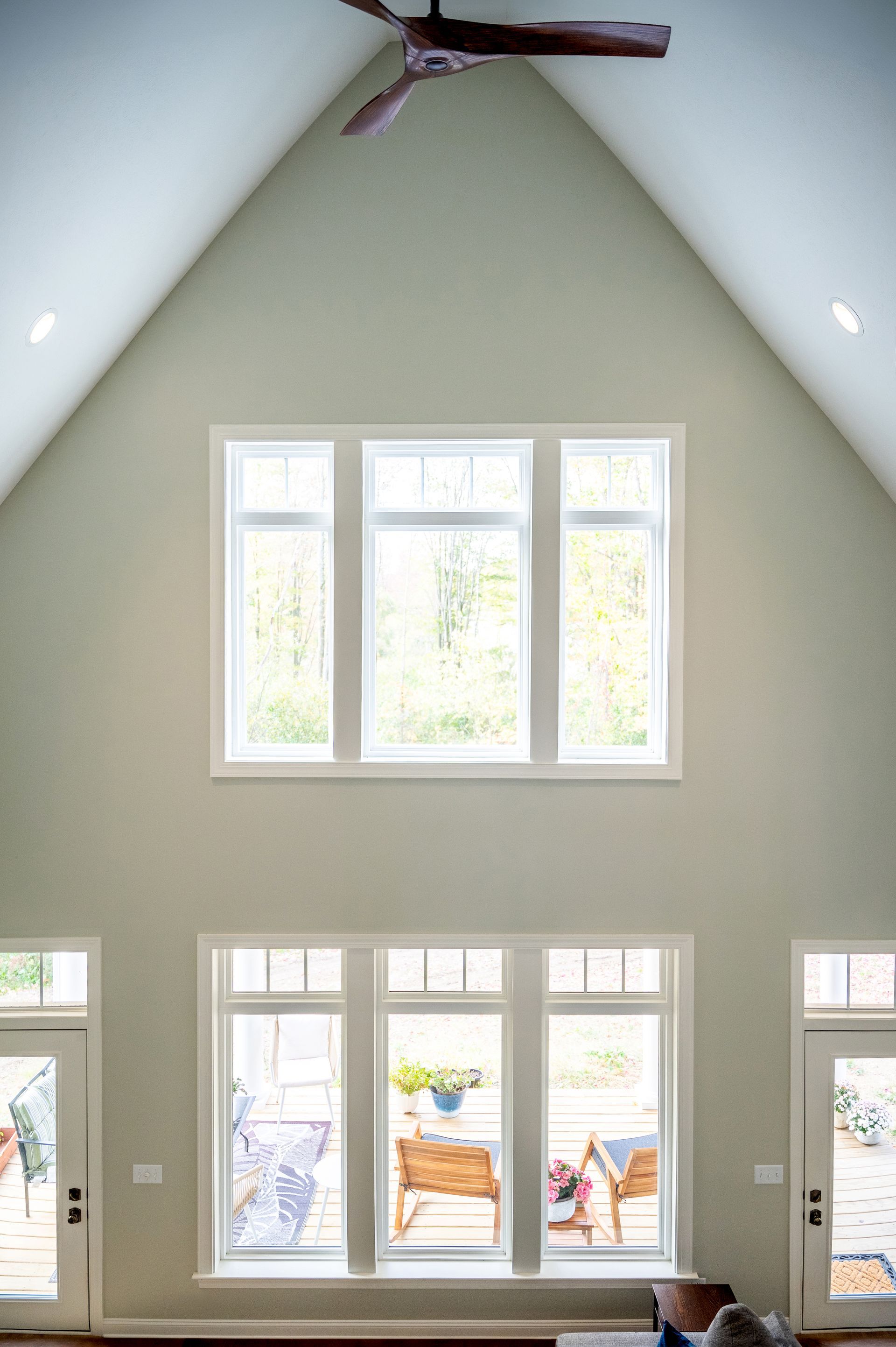 Interior view of a bright room with high ceilings and large windows. Light green walls, white window frames, and a ceiling fan.