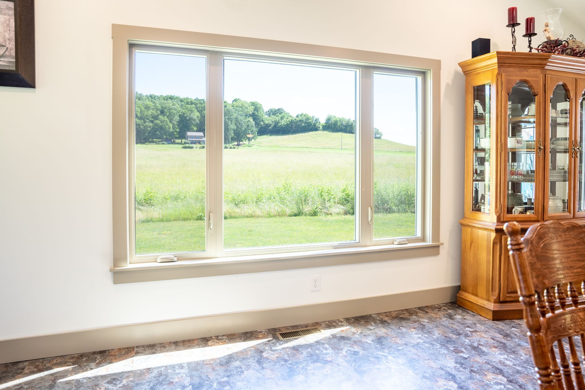 Window overlooking a green field. A wooden cabinet and part of a chair are in the room.