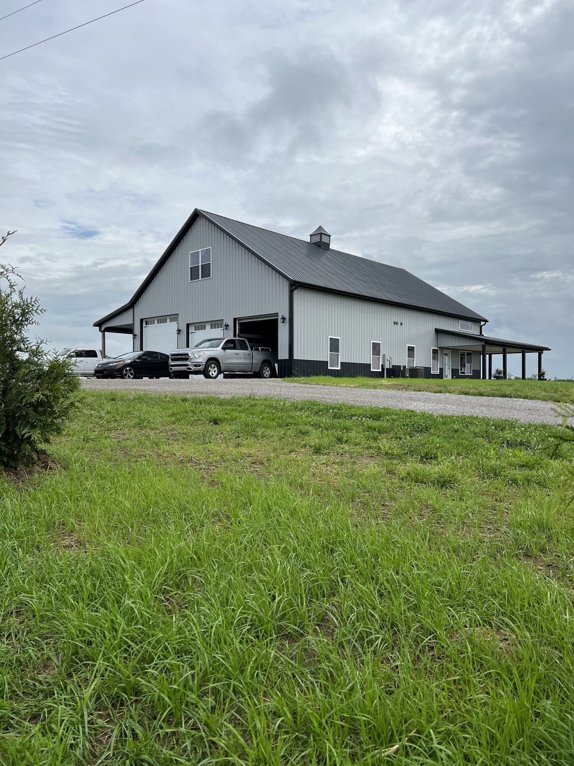 A large, white barn with a black roof and trim, set in a grassy field under an overcast sky. A truck is parked inside.