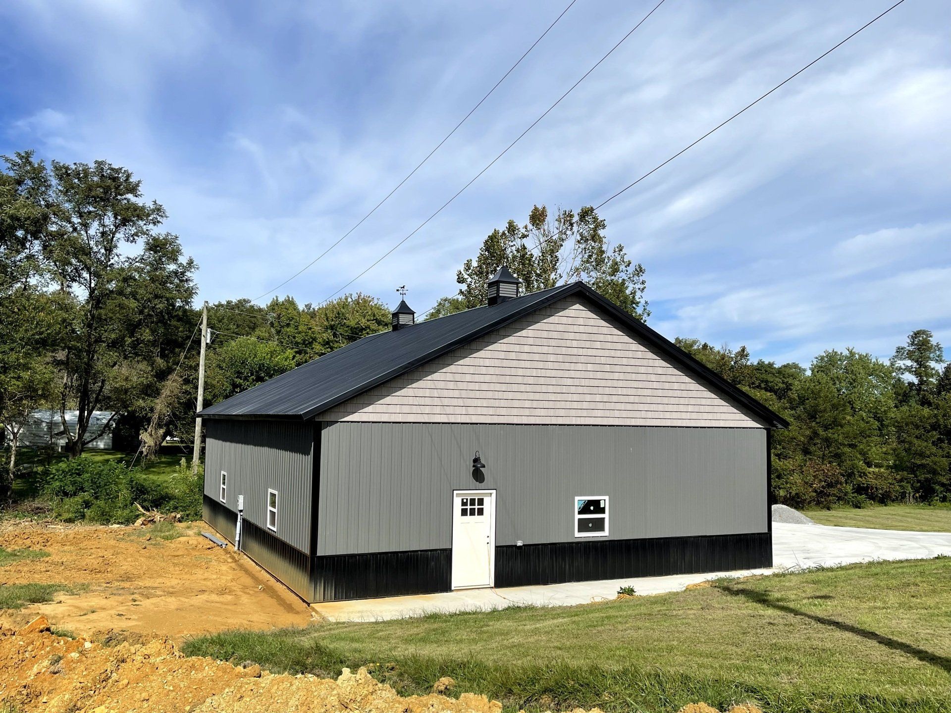 Gray and black barn-style building with a dark roof, white door, and small windows against a blue sky.