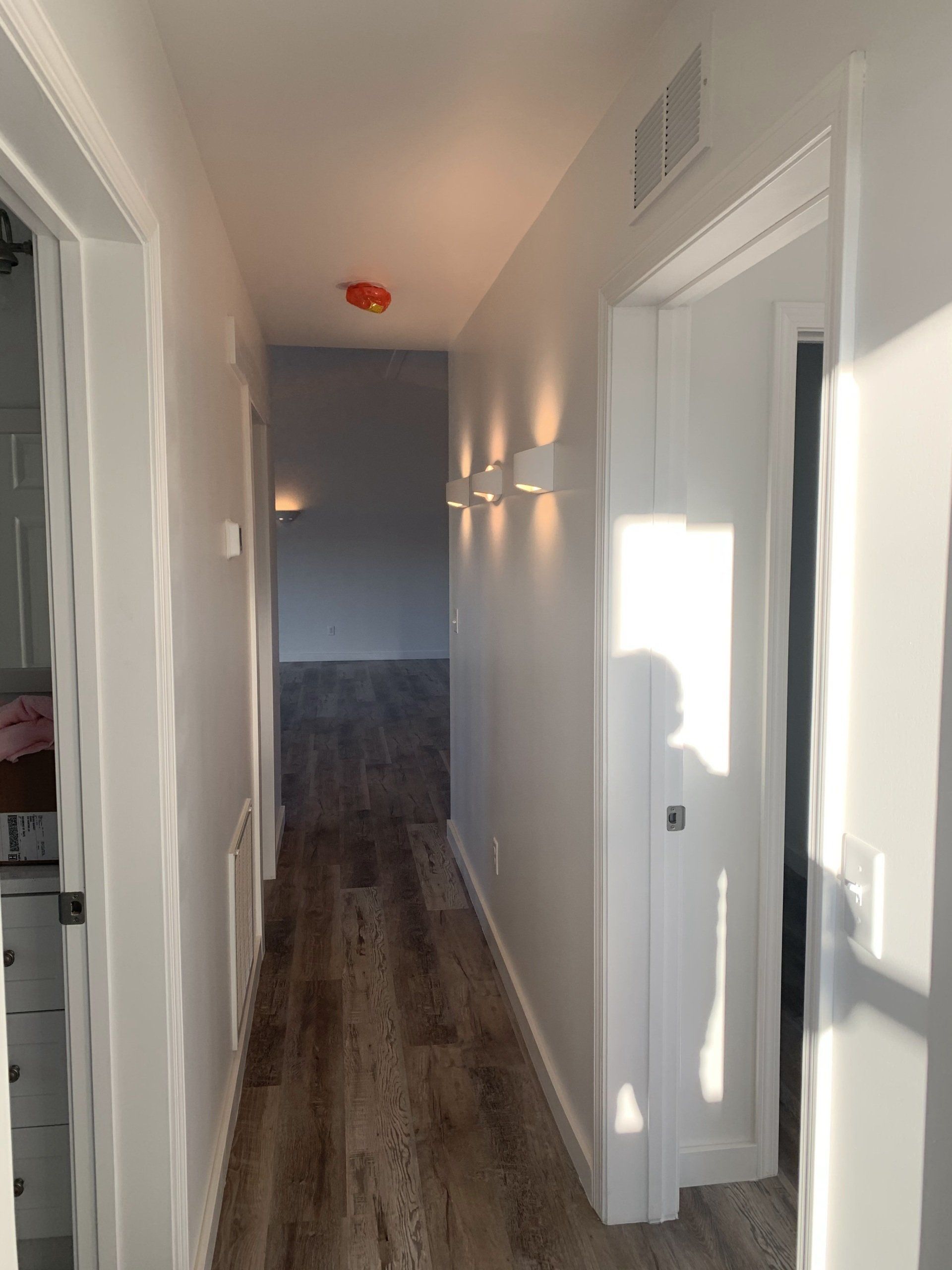 Narrow hallway with light-colored walls, wood-look flooring, and three sconce lights. Doors line either side.