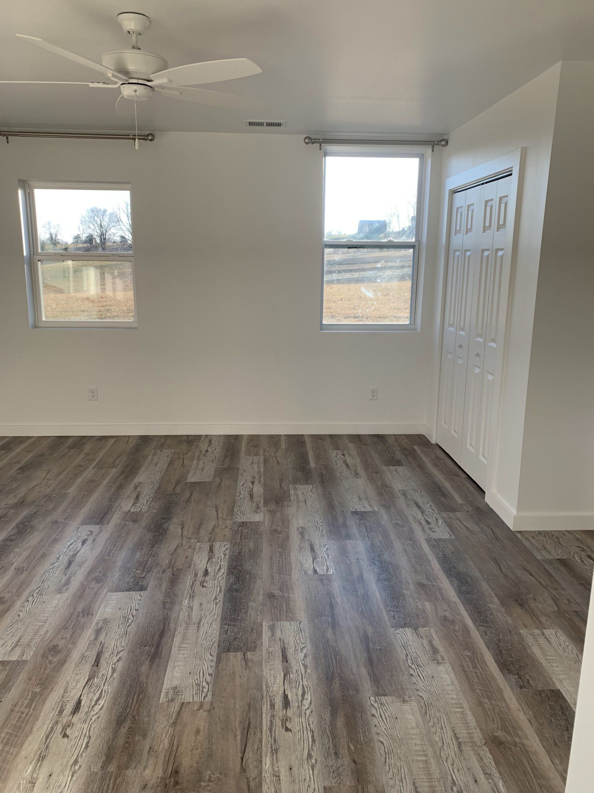 Empty room with wood-look flooring, white walls, two windows, and a white ceiling fan.