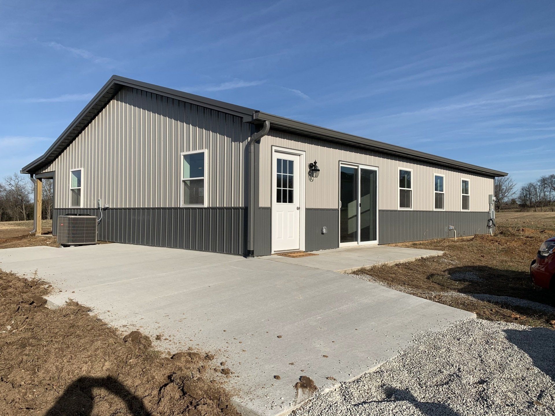 A long, light-gray and dark-gray metal building with a concrete driveway on a sunny day.