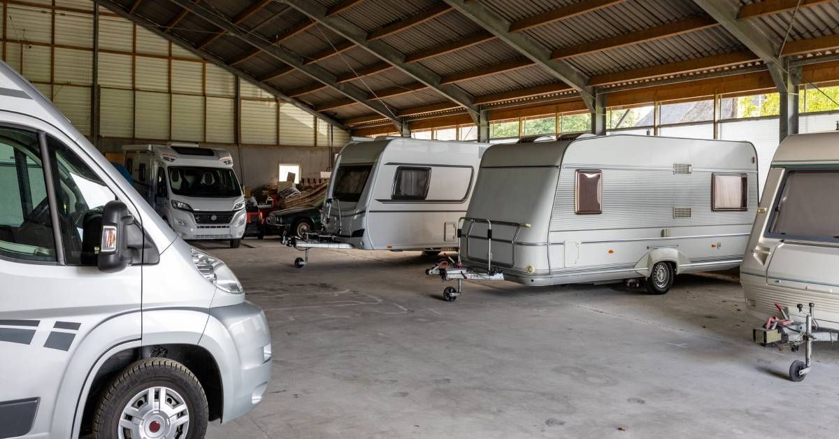 Several RV trailers stored in a barn with protection from the outdoors. The RVs are mainly white wit