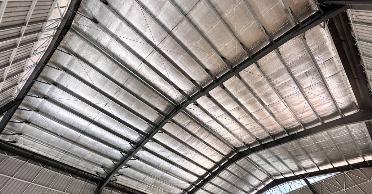 An upward view of the inside of a barn, looking up at the metal roof and the components that make up its metal framework.