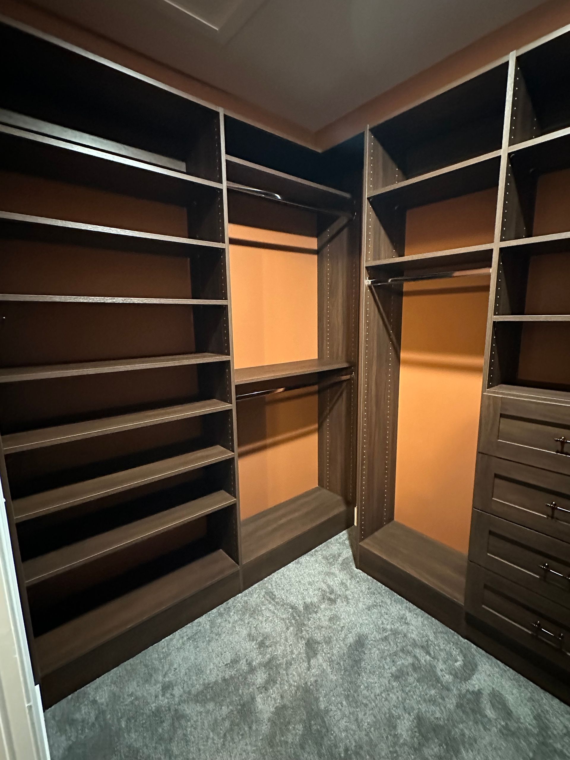 Walk-in closet with dark wood shelving and a light orange backdrop. The carpet is gray.
