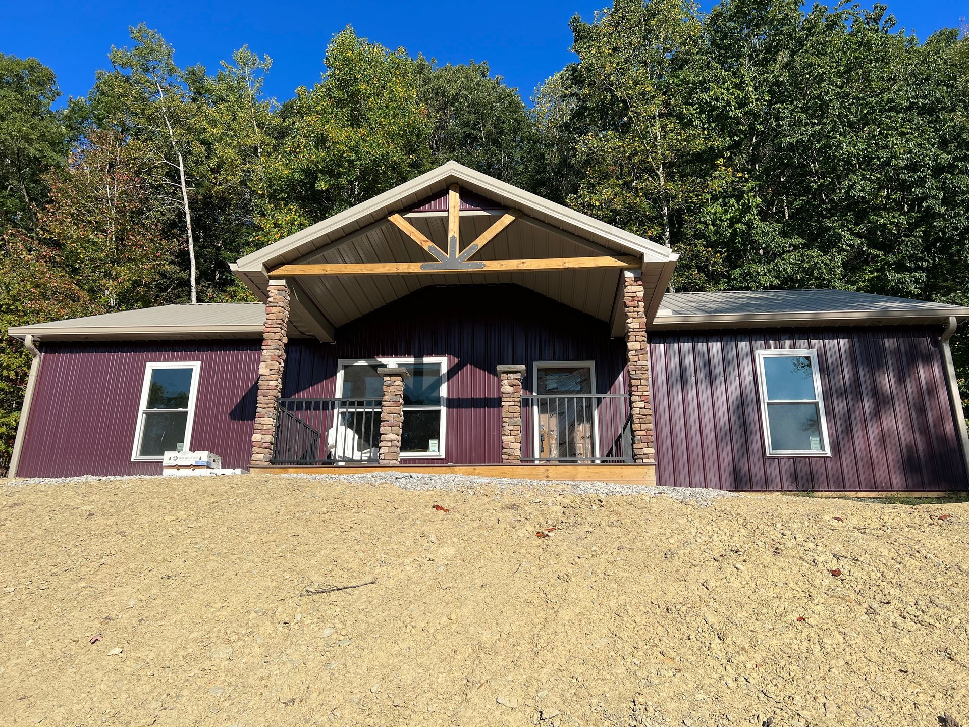 A dark purple house with a small porch and decorative stone pillars, set against a backdrop of trees.