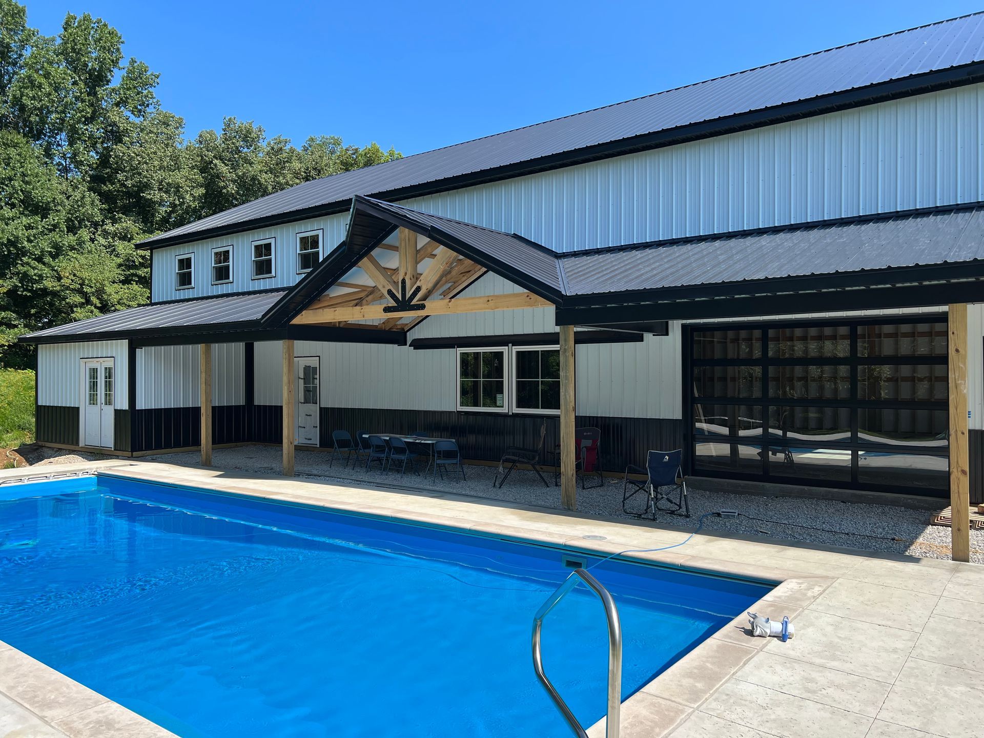 A large white and black building with a pool in front. The pool has a blue cover, and there is a patio area with tables and chairs.