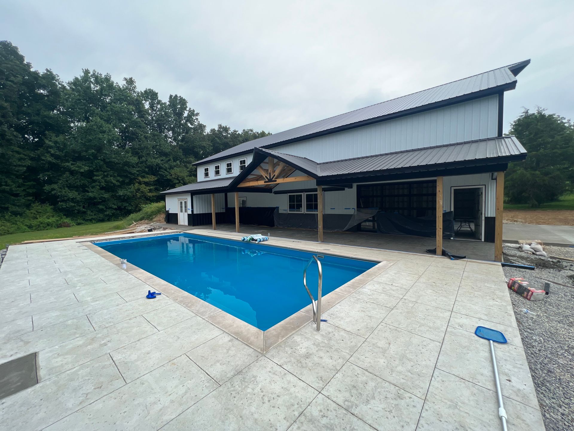 A two-story white building with a black roof and a pool with bright blue water. The building has a covered patio.