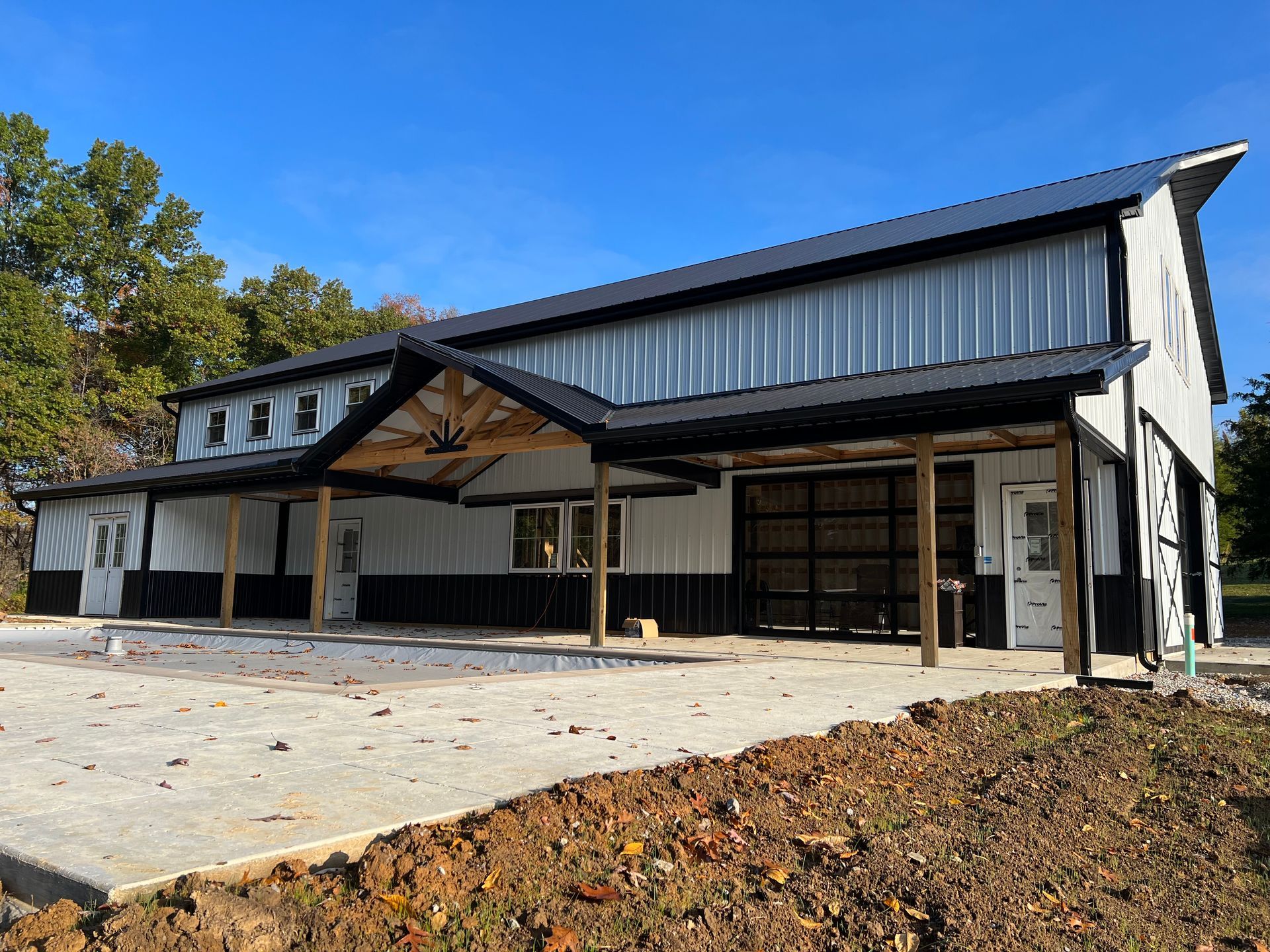 A modern barn-style building under construction with a black roof, white and black siding, and a concrete pad.