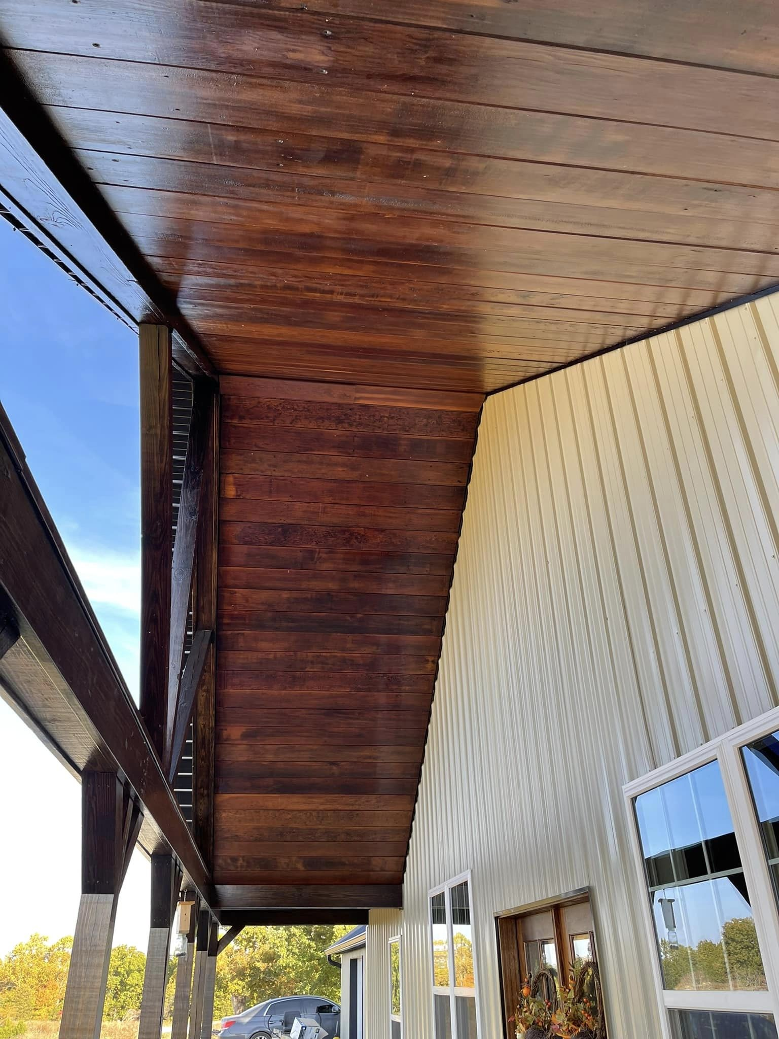 Wooden porch ceiling with a rich, dark stain, next to a cream-colored wall with windows.